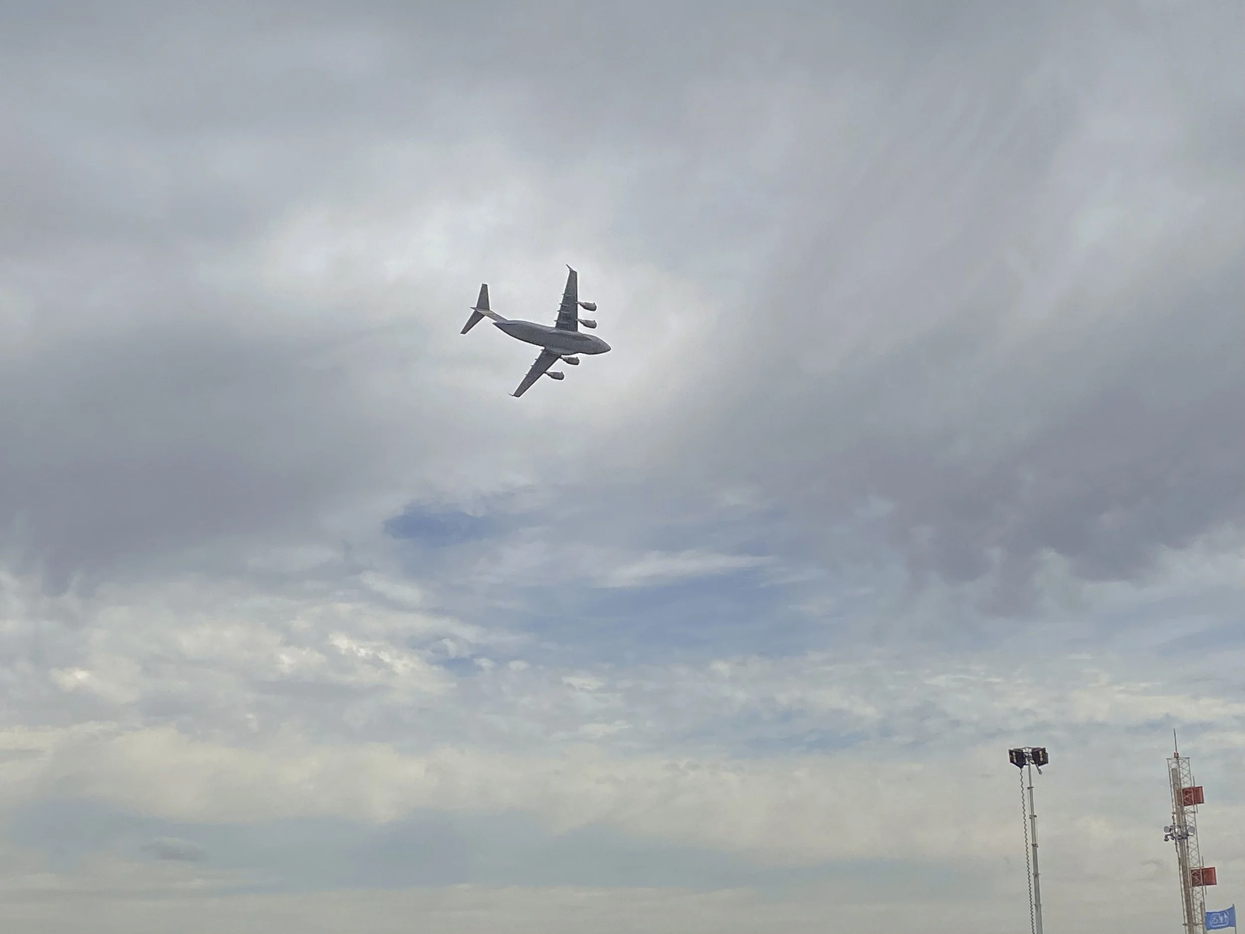 A commercial airplane flying through a cloudy sky near airport lights and antennas.