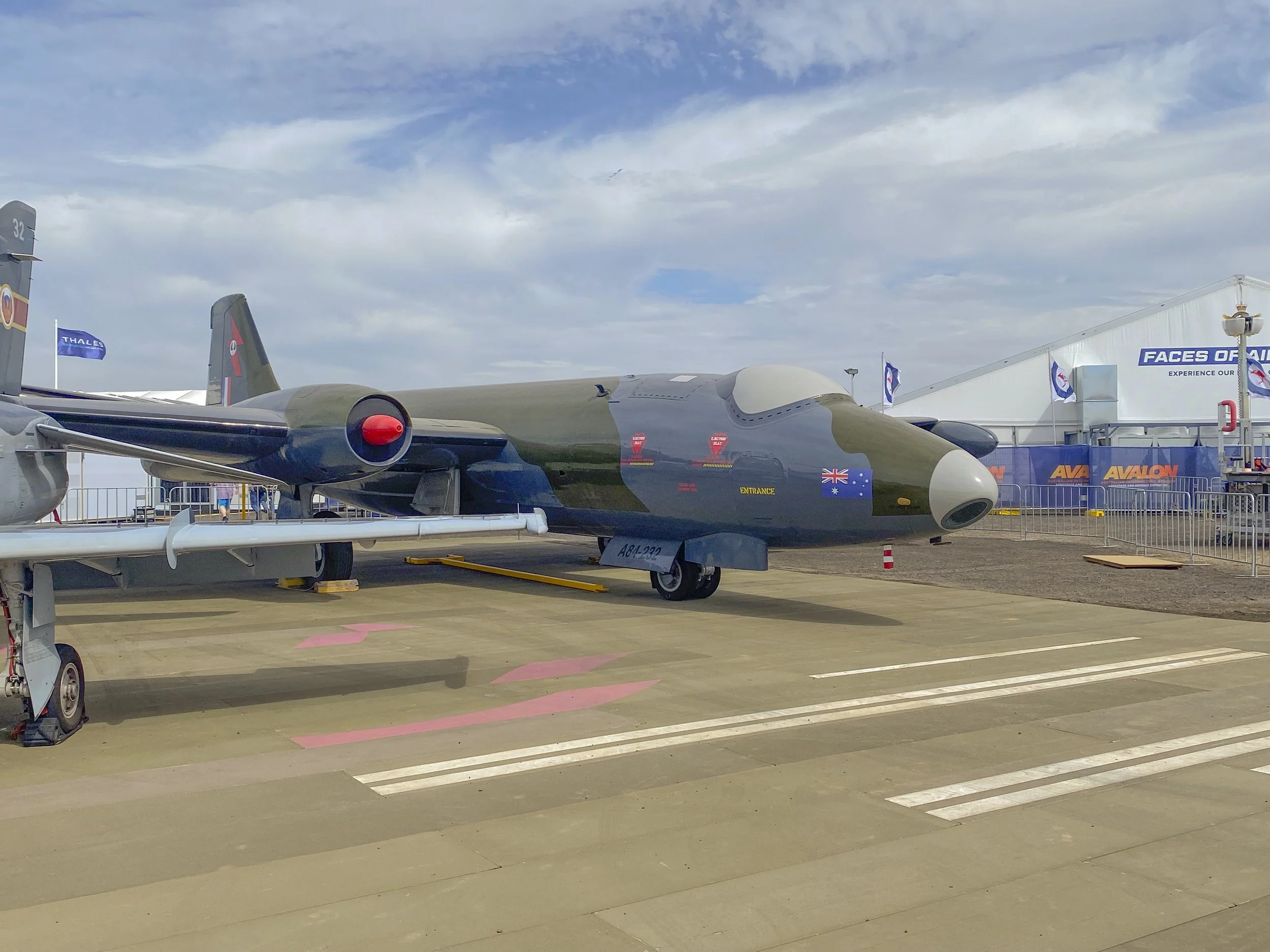 Military jet aircraft displayed at an outdoor aviation event, with surrounding barriers and event tents in the background.