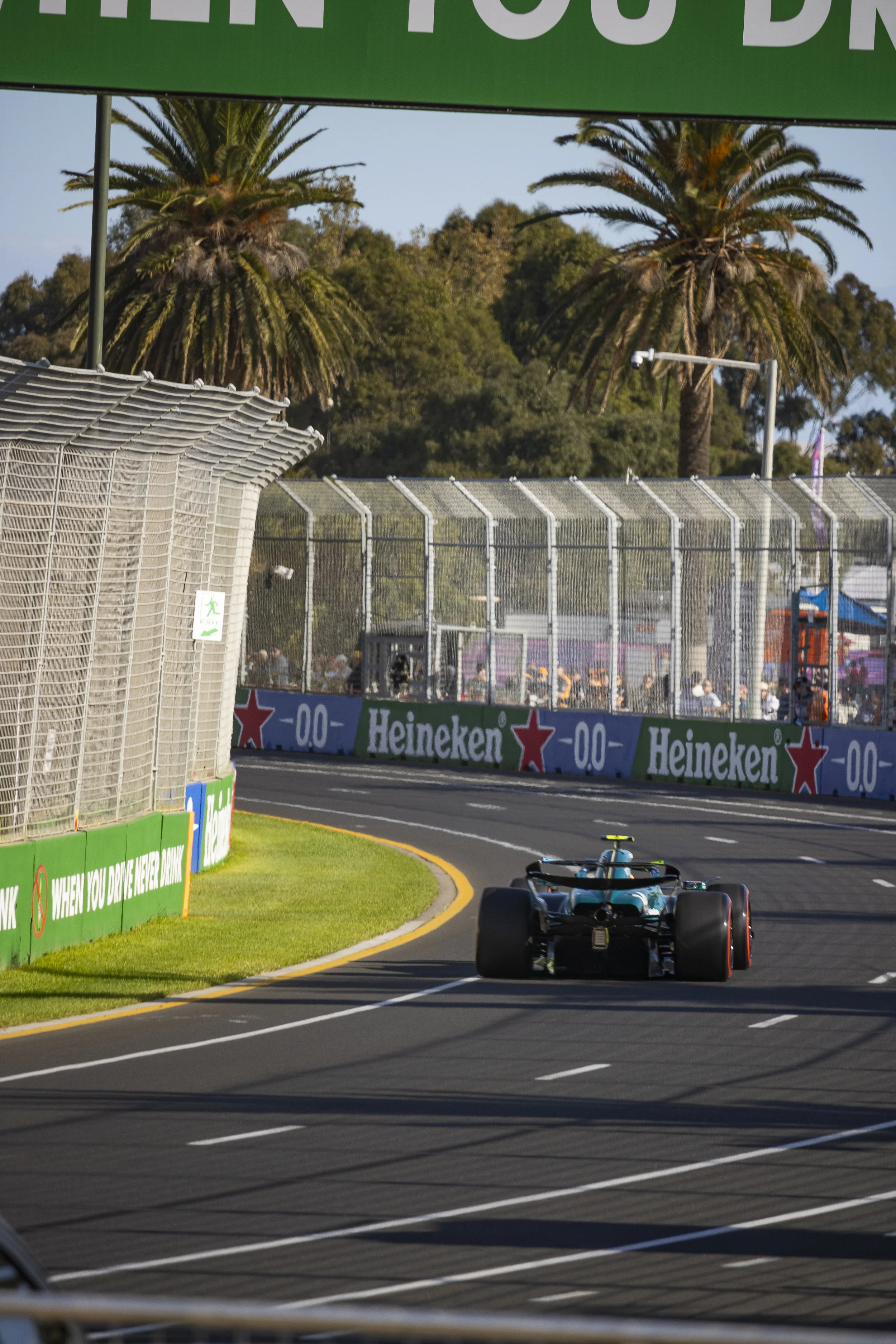 A racing car on a track, speeding past the 100 meters sign, with palm trees and a crowd of spectators in the background.