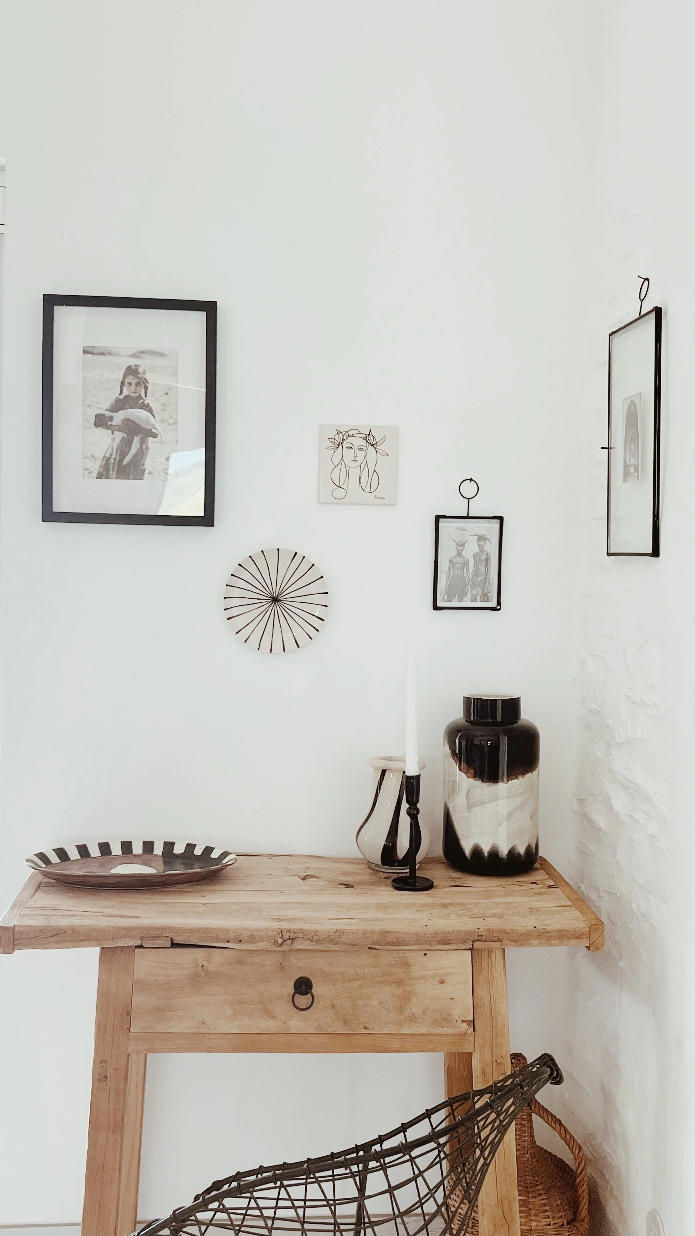 Intérieur minimaliste avec un mur blanc, une table en bois, des décorations murales en noir et blanc, un vase noir, une bougie et un plat décoratif