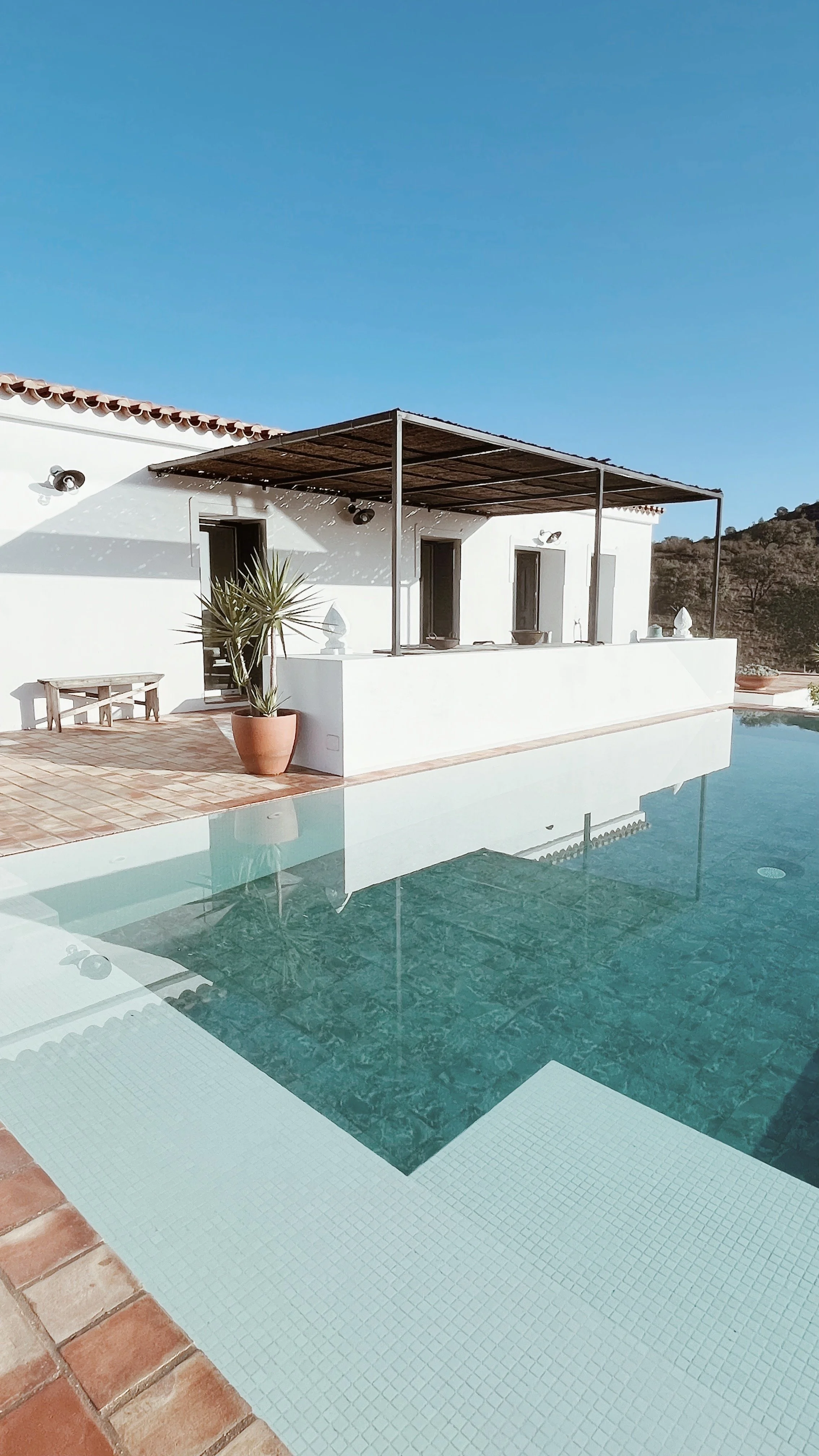 Piscine extérieure avec une villa blanche moderne, un espace terrasse, un parasol, et un paysage de montagnes en arrière-plan.