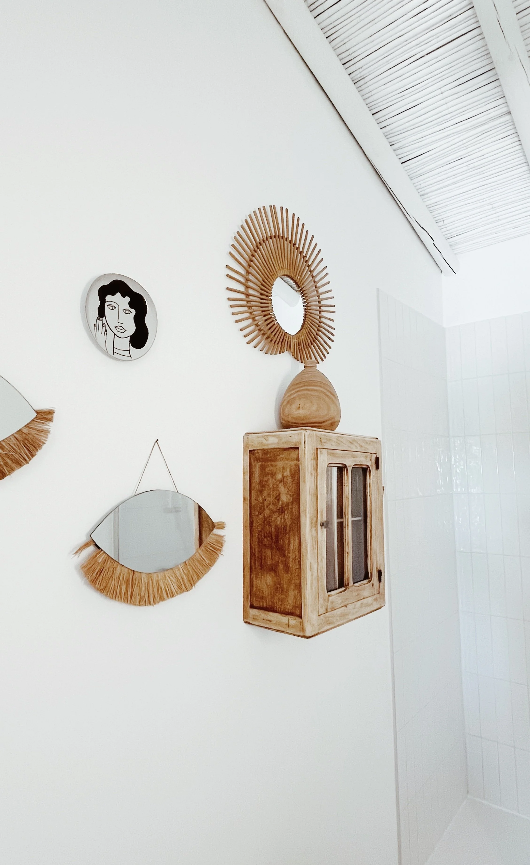 Mur blanc décoré de miroirs et d'une pièce en bois, avec un père sur le mur et un miroir rond avec un cadre en bois en forme de soleil.