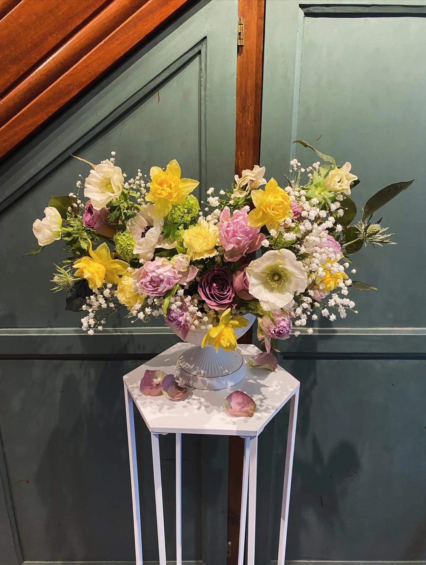 Un bouquet de fleurs colorées, comprenant des roses, des pivoines, des œillets et des fleurs de gypsophile, placé dans un vase blanc sur une petite table blanche.