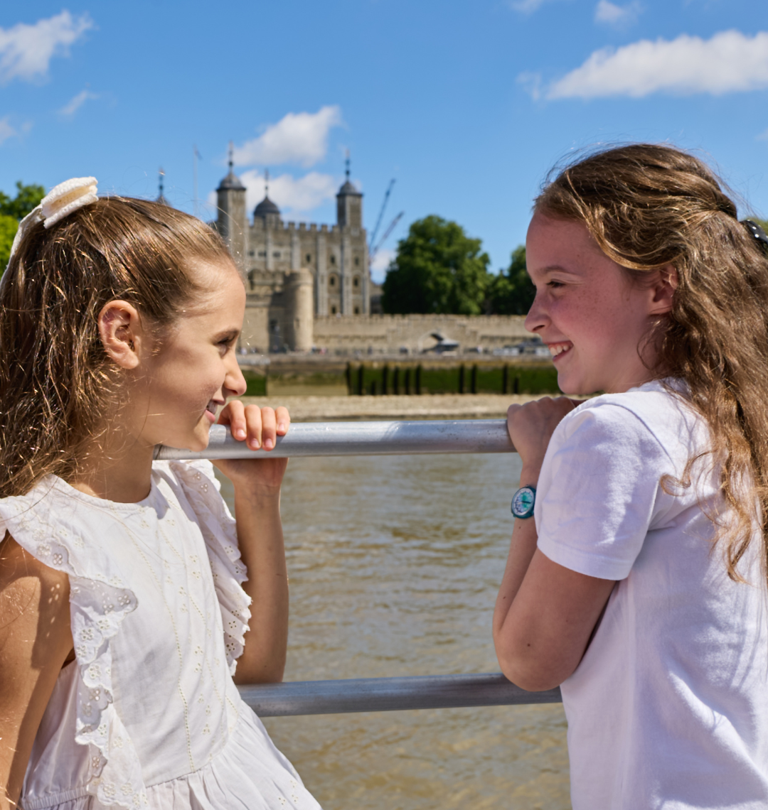 Two children enjoying a River Thames cruise with the Tower of London in the background on a sunny day in London.