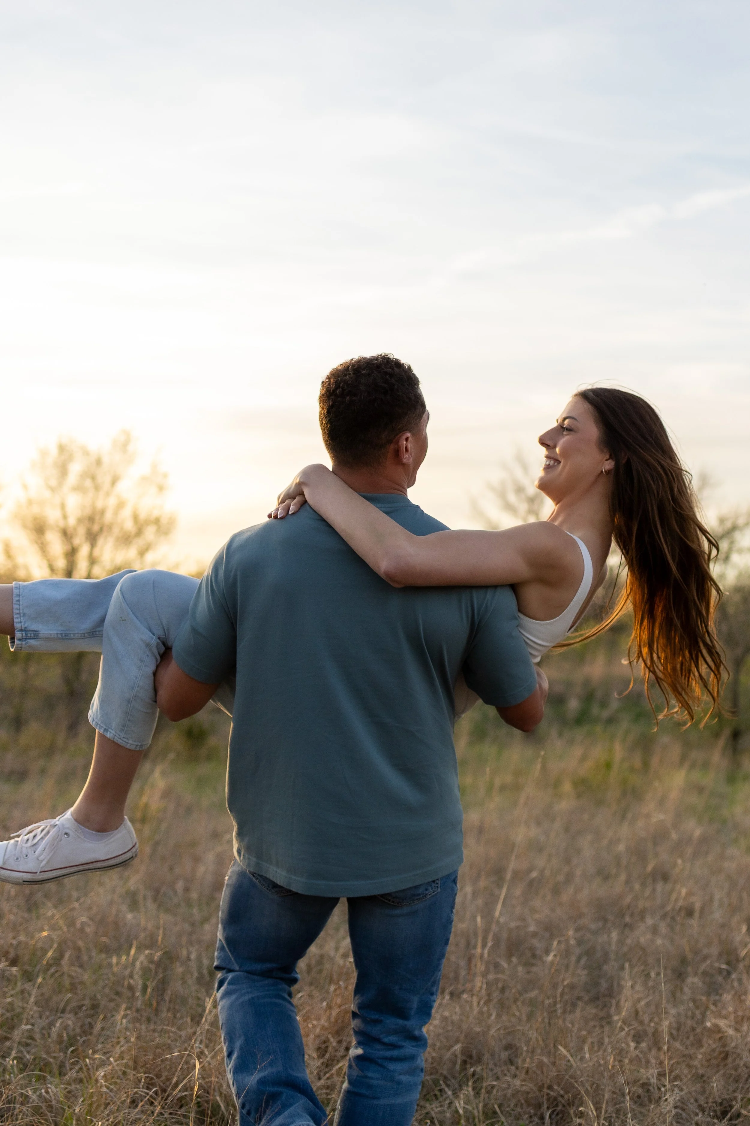 A couple walking through a field, the man holding the woman in his arms during a couples photography session in wichita, ks