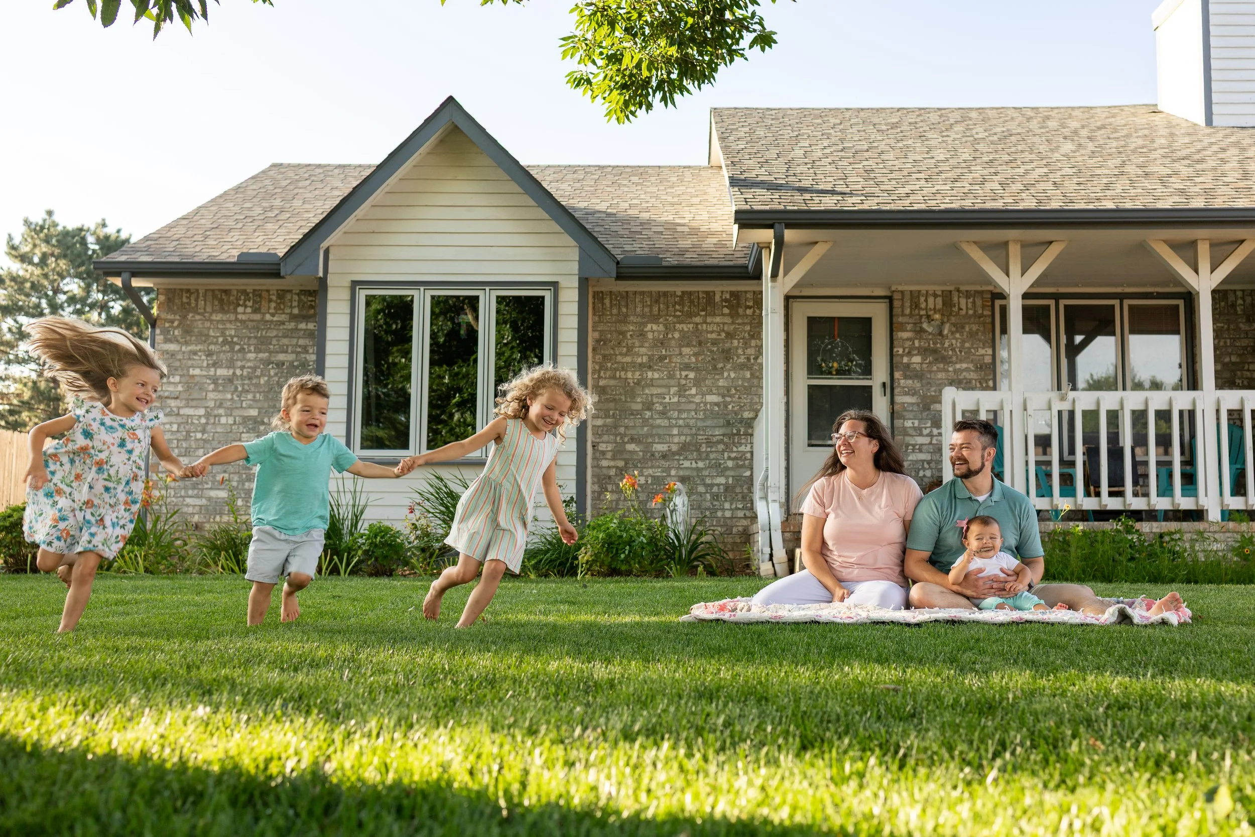 Children and parents playing and sitting on the grass in front of their home for a Backyard Summer Session in Wichita, KS