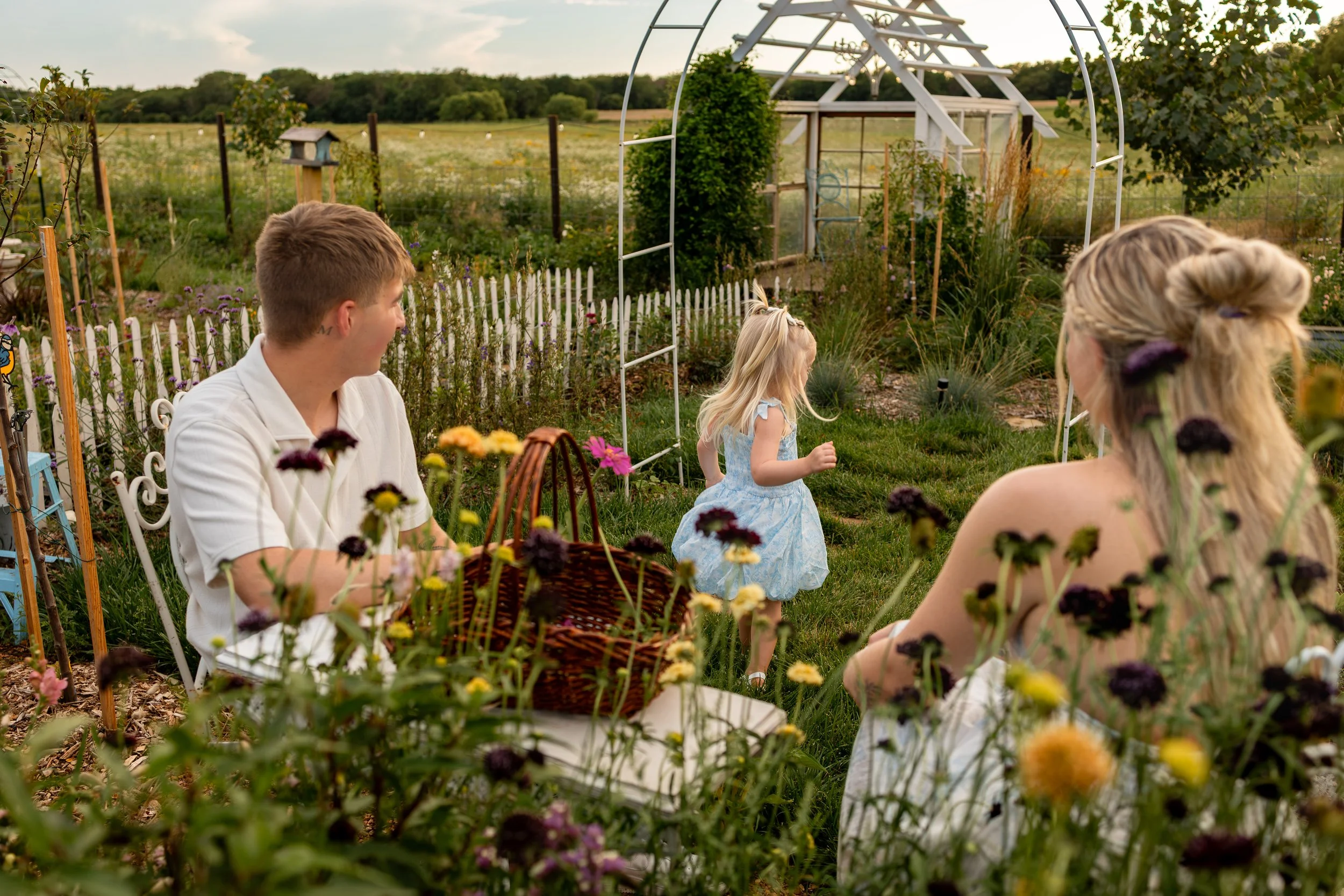 little girl dancing in the flowers with parents lovingly watching her for family photo session wichita Kansas