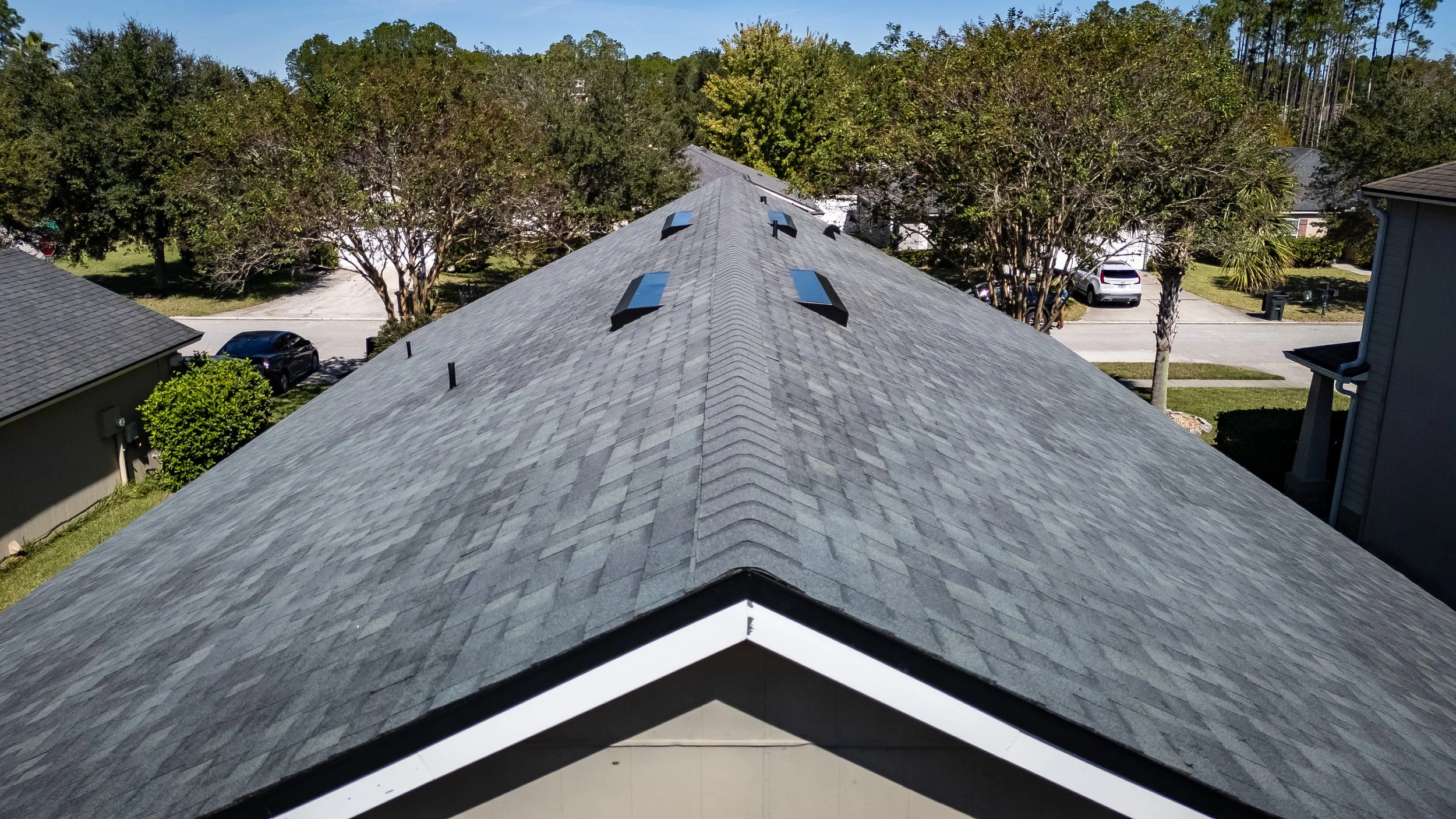 Newly installed gray architectural shingle roof on Florida residential home with roof vents and skylights in suburban neighborhood.