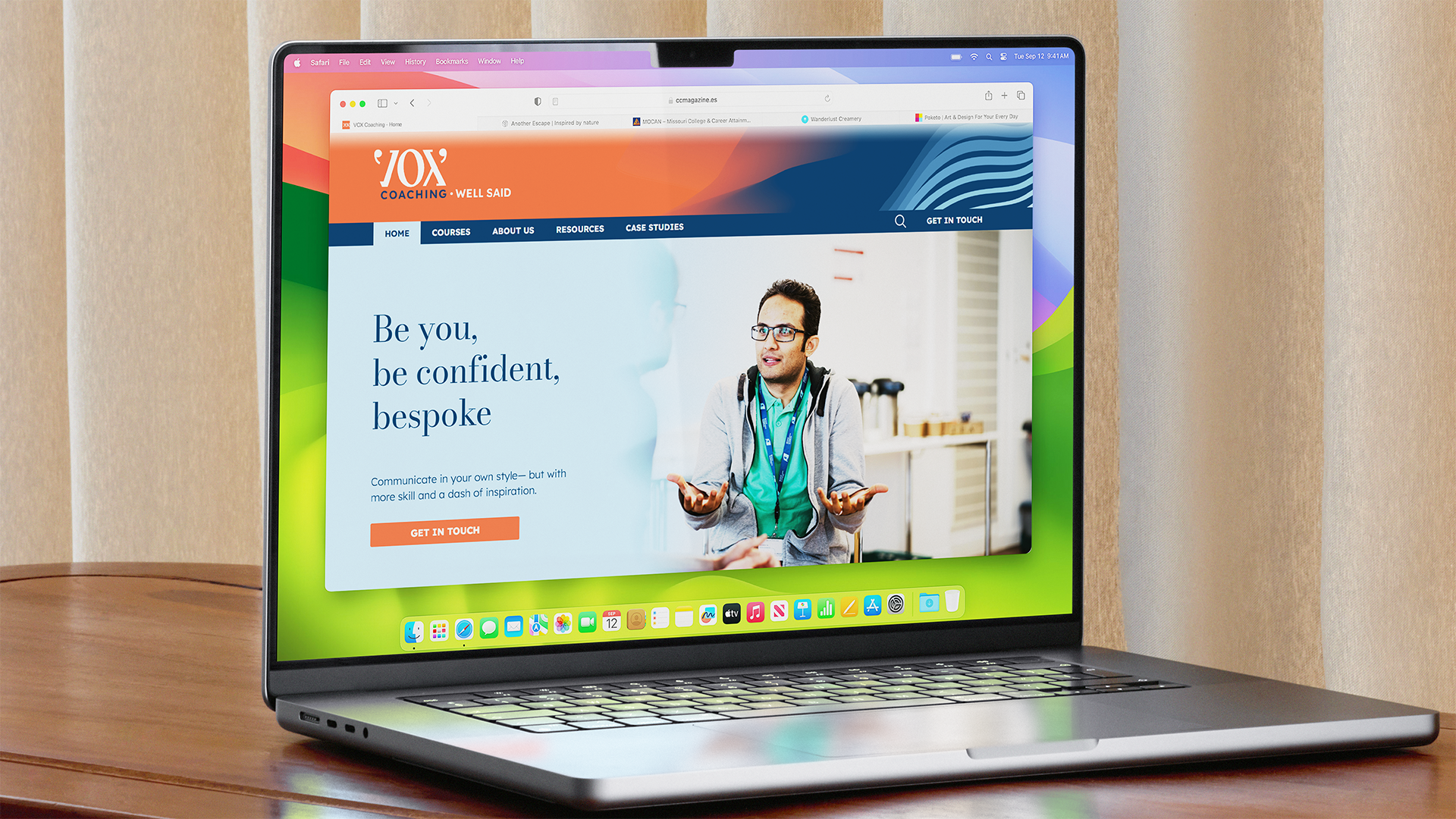 A MacBook laptop displaying a coaching website with a man gesturing with his hands, wearing glasses, and a green shirt. The background of the website has the text 'Be you, be confident, bespoke' and a 'Get in Touch' button.