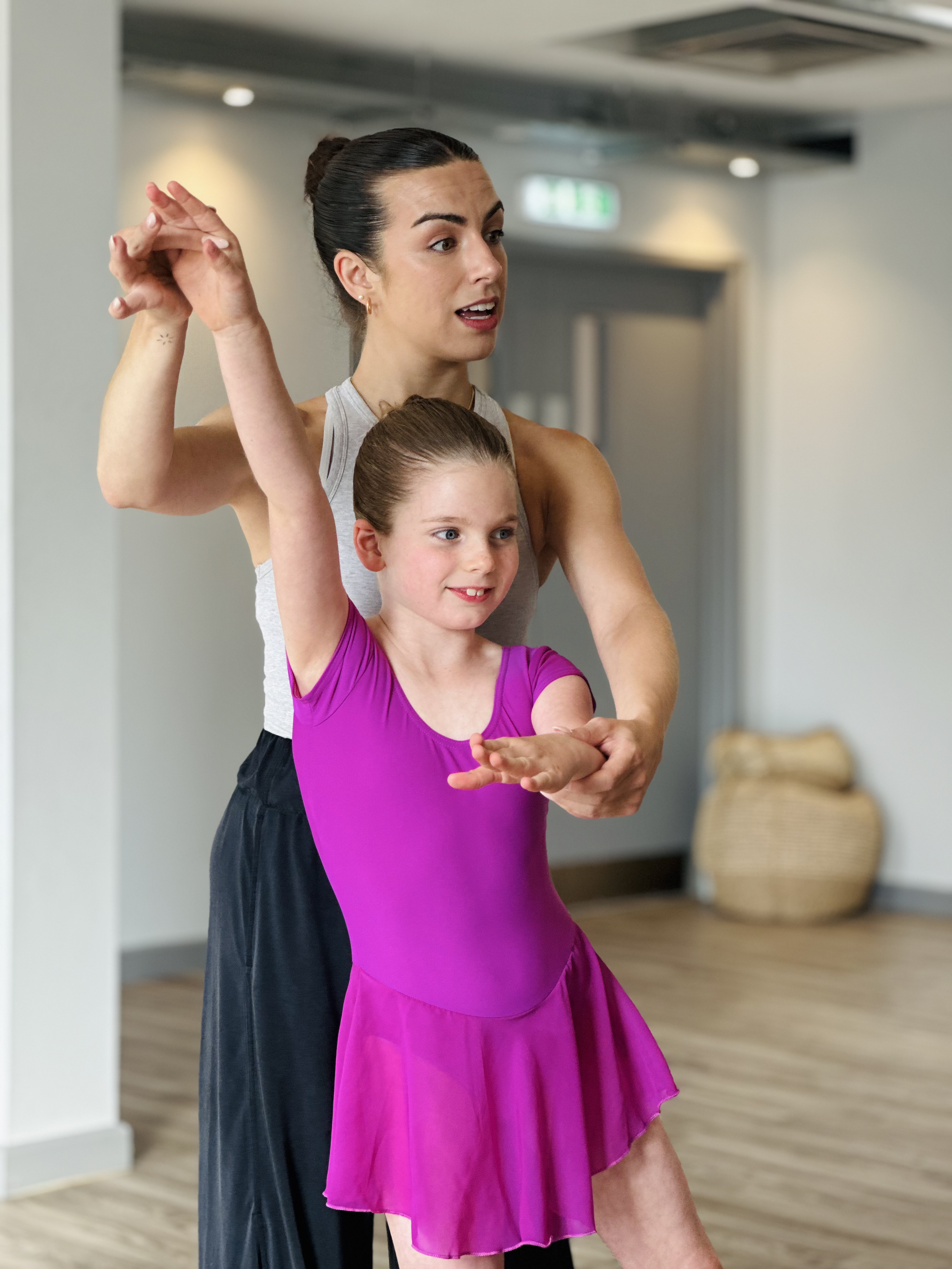 A ballet instructor helping a young girl practice ballet moves in a dance studio.