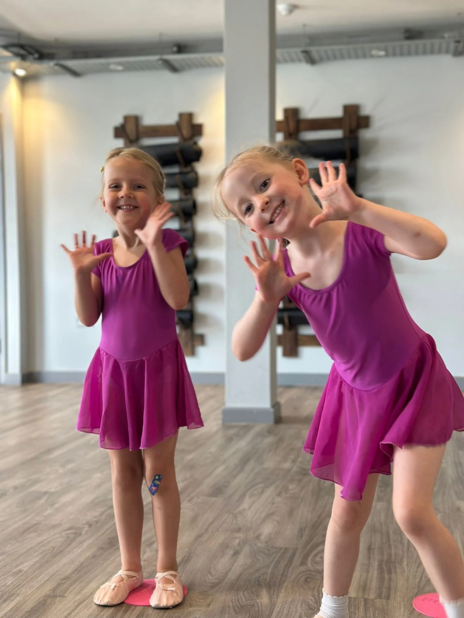 Two young girls in pink ballet dresses playing and smiling in a dance studio.