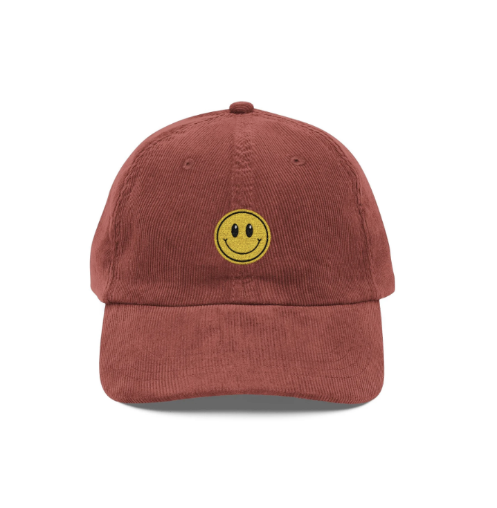 Red baseball cap with a yellow smiley face patch on the front.