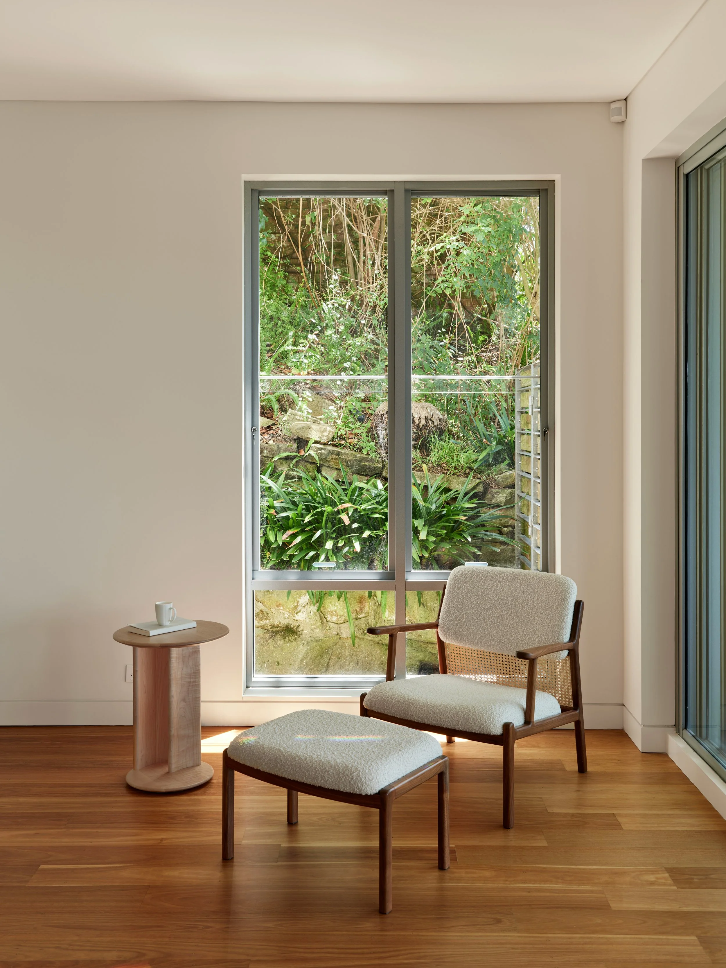 chair in the corner of room with small side table and large window with plants outdoors