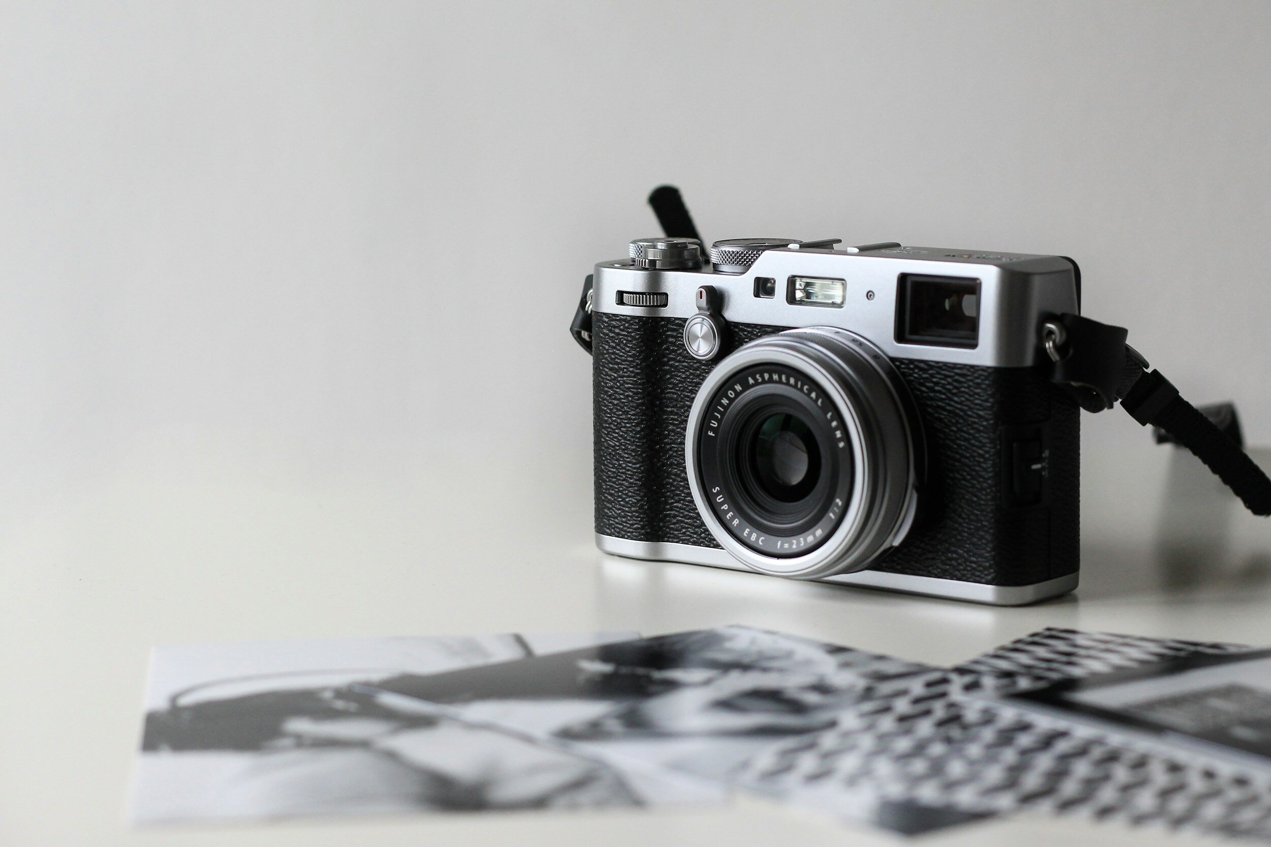 A vintage-style film camera with a strap beside black and white photographs on a white surface.