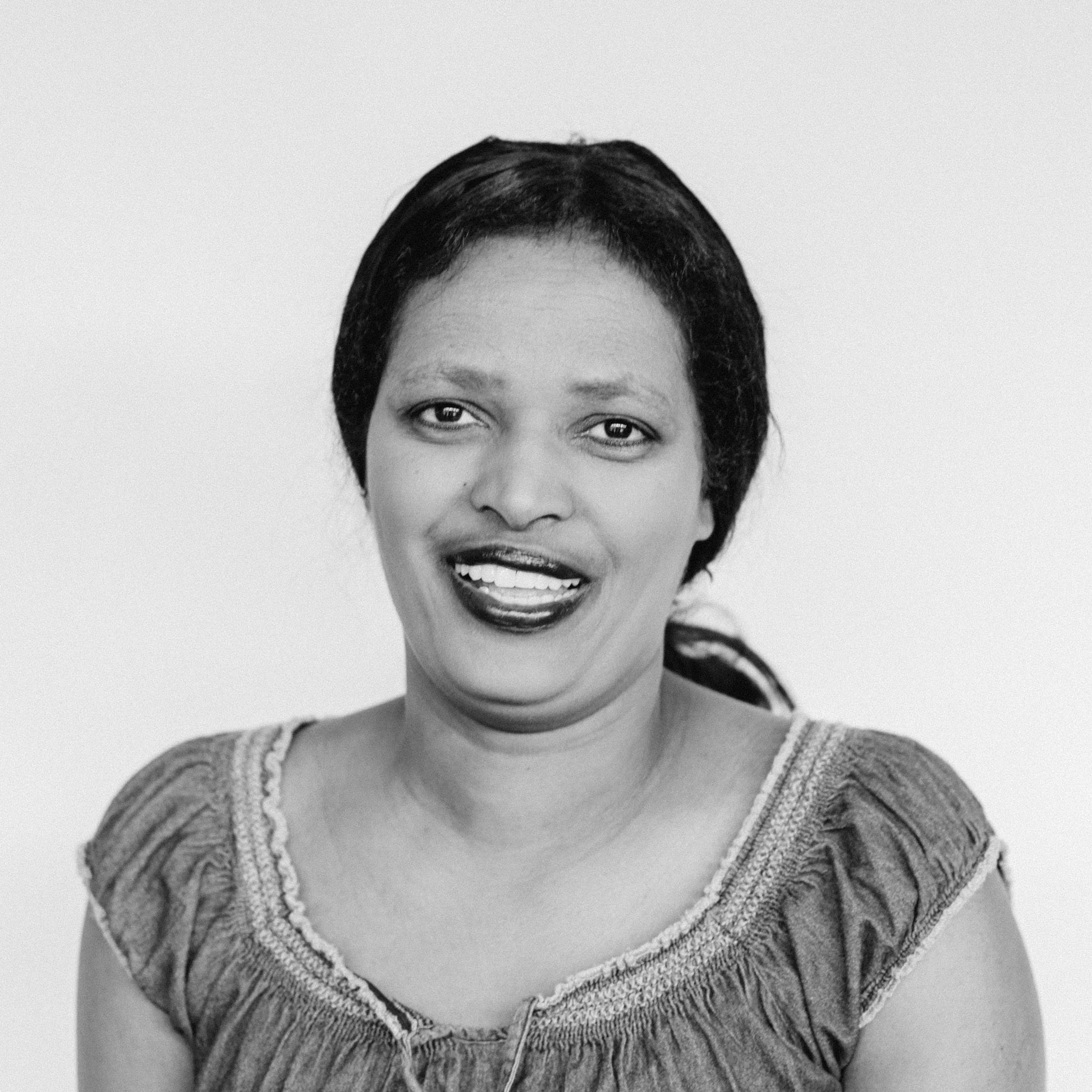 A smiling woman with medium-dark skin tone wearing her black hair pulled back in a low ponytail and a textured top with embroidery details.
