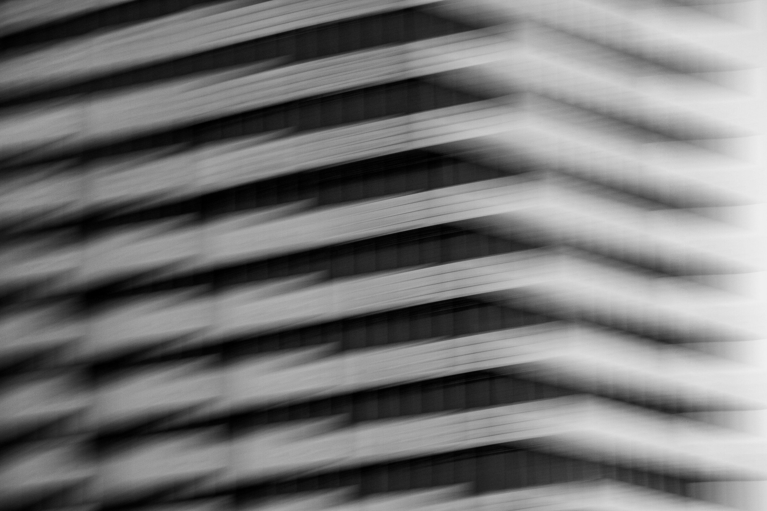 Close-up black-and-white photo of a modern building's facade with horizontal lines and a blurred effect.
