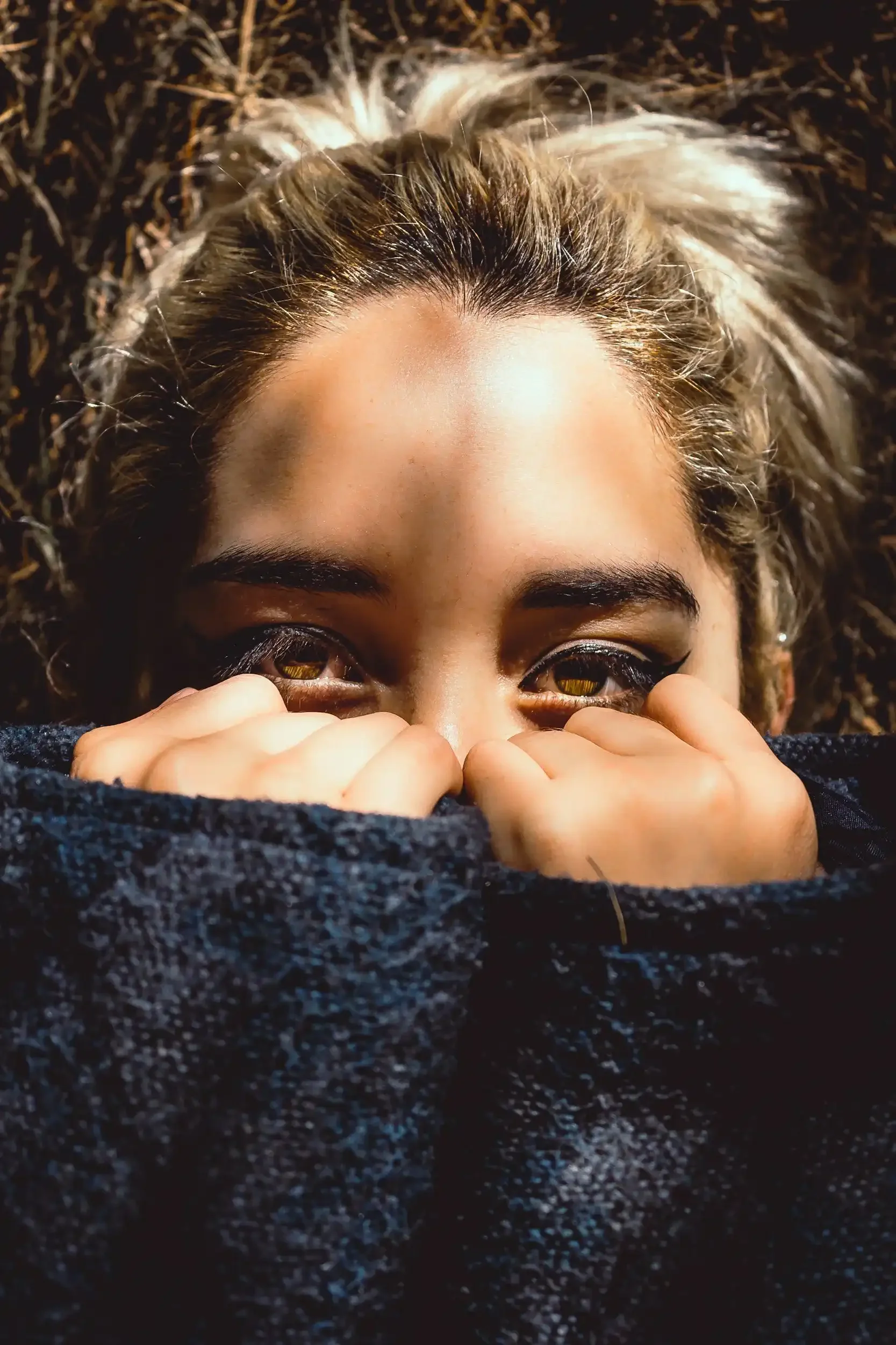 Close-up of a woman’s eyes peeking over a sweater, with warm natural lighting and a soft outdoor background.