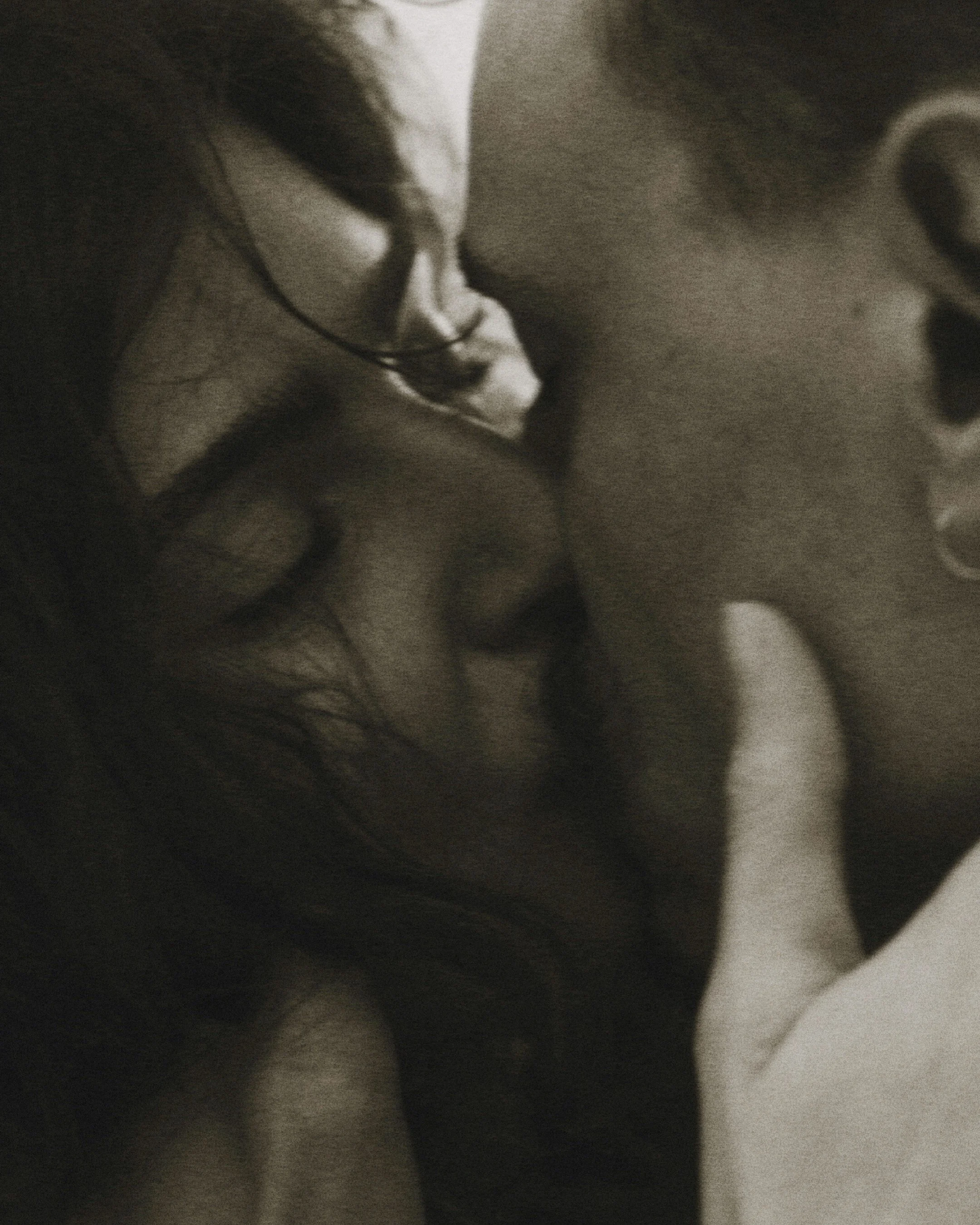 Close-up of a person's face with glasses, showing only part of their face in a subdued, grayscale tone.