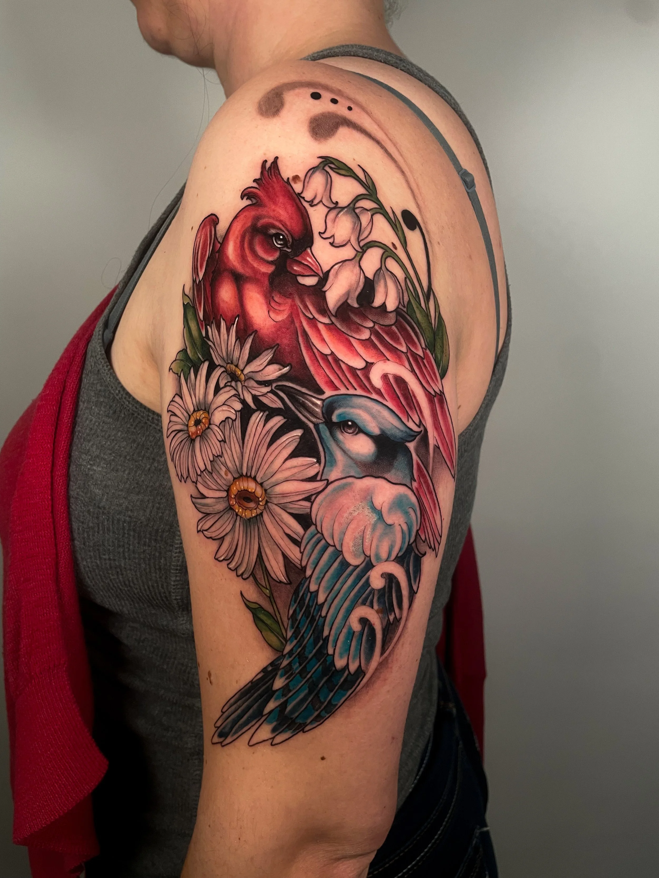 Tatouage coloré de deux oiseaux et de fleurs sur le bras d'une personne.