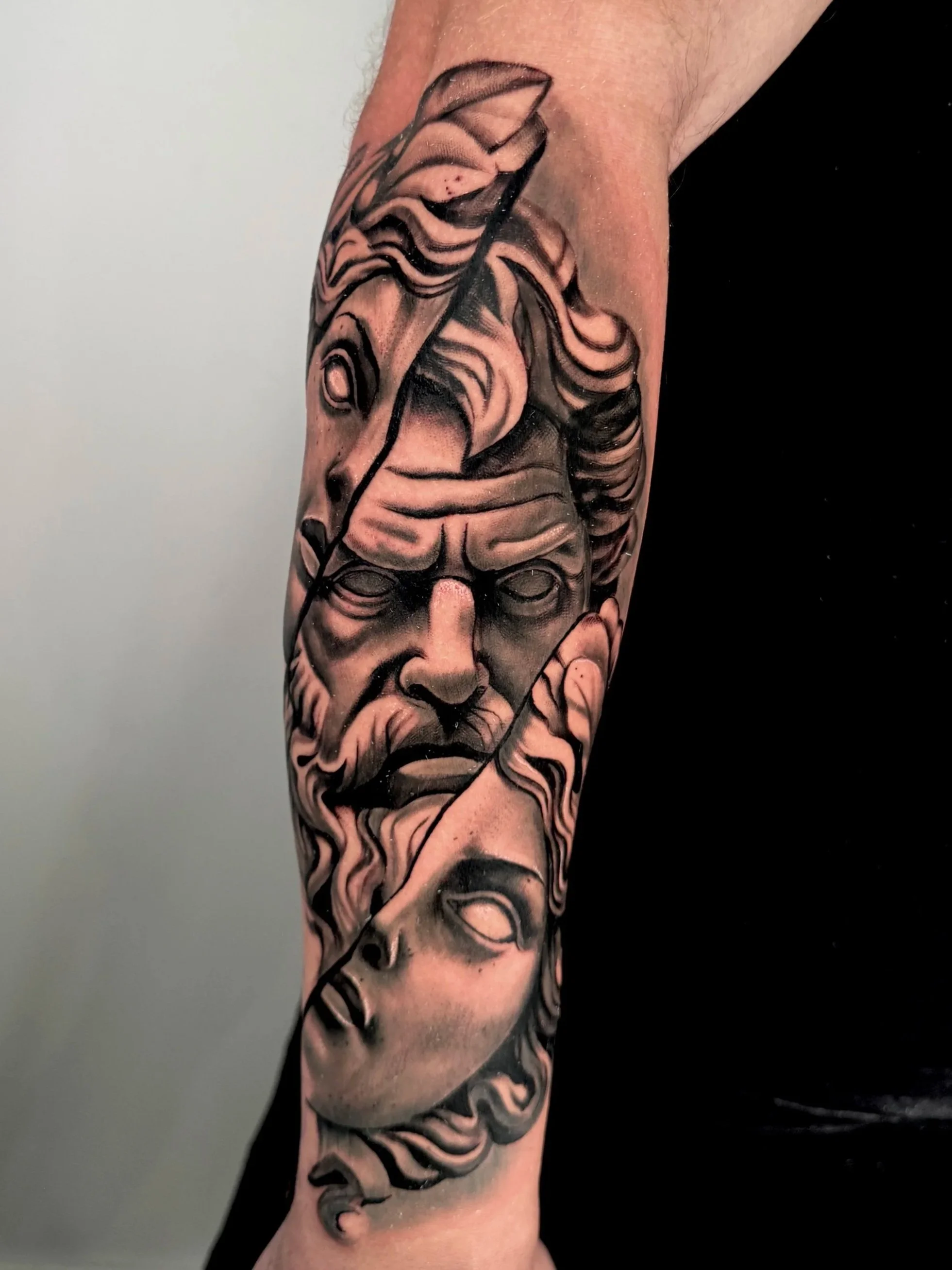 Tattoo of a human face with stylized details in black and gray on the arm