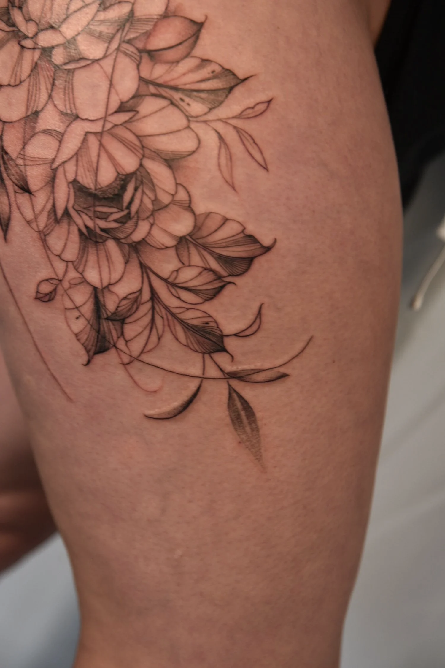 Tattoo of flowers and leaves in black lines on the skin.
