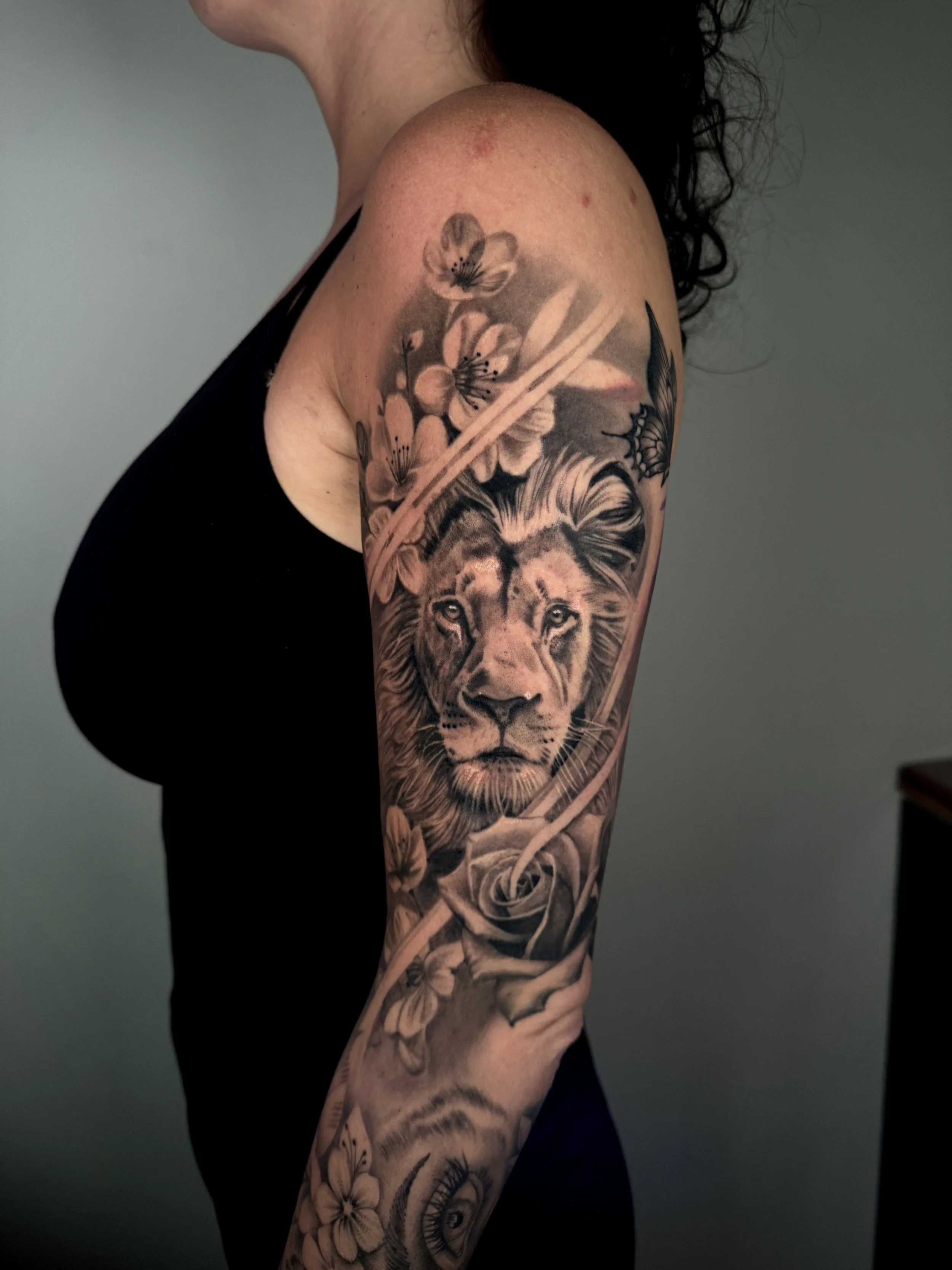 A tattoo on a woman's arm, featuring a lion, flowers, a butterfly, and a cherry blossom branch