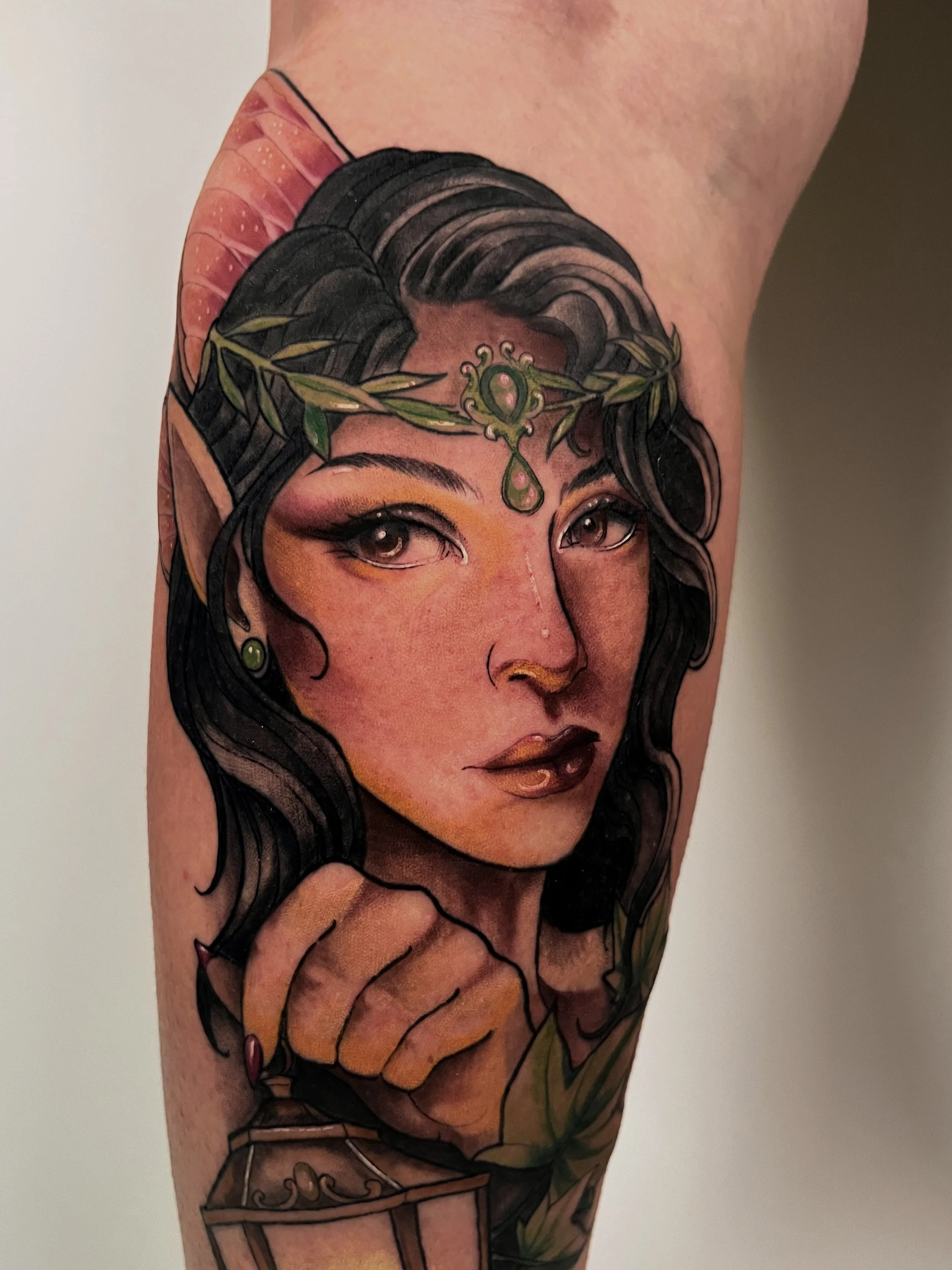 Tattoo of an elven woman with black hair, wearing a crown of leaves and green jewels, with a jewelry box underneath.