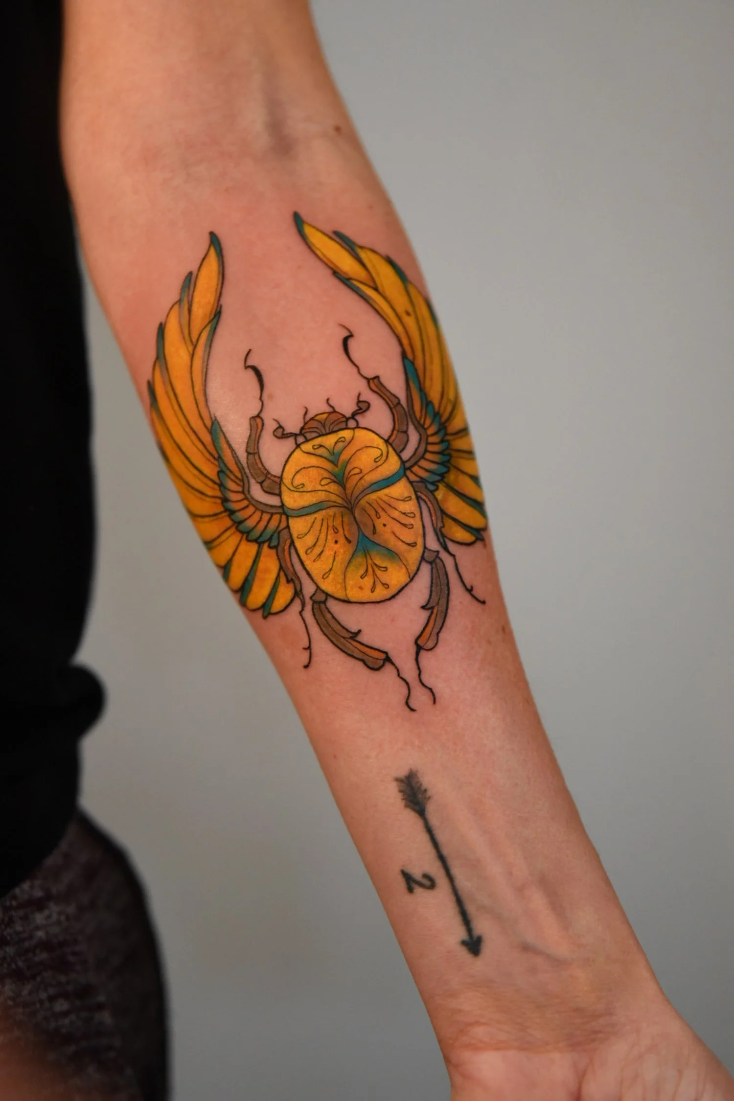 Tattoo of an orange and yellow colored beetle with spread wings on the arm