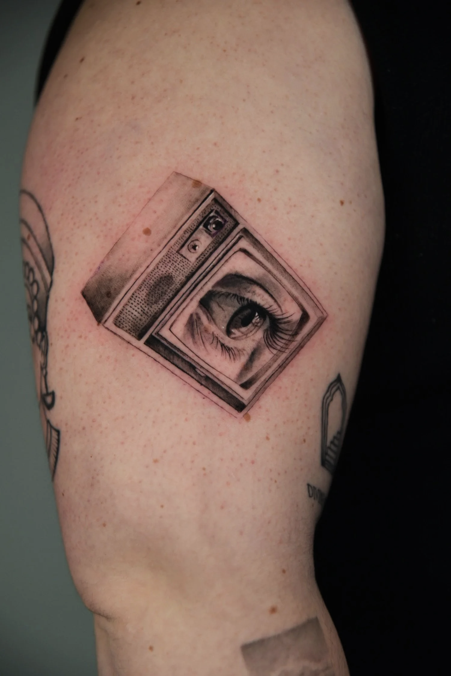 Realistic tattoo of a television frame, with a human eye in the screen, on a person's arm.