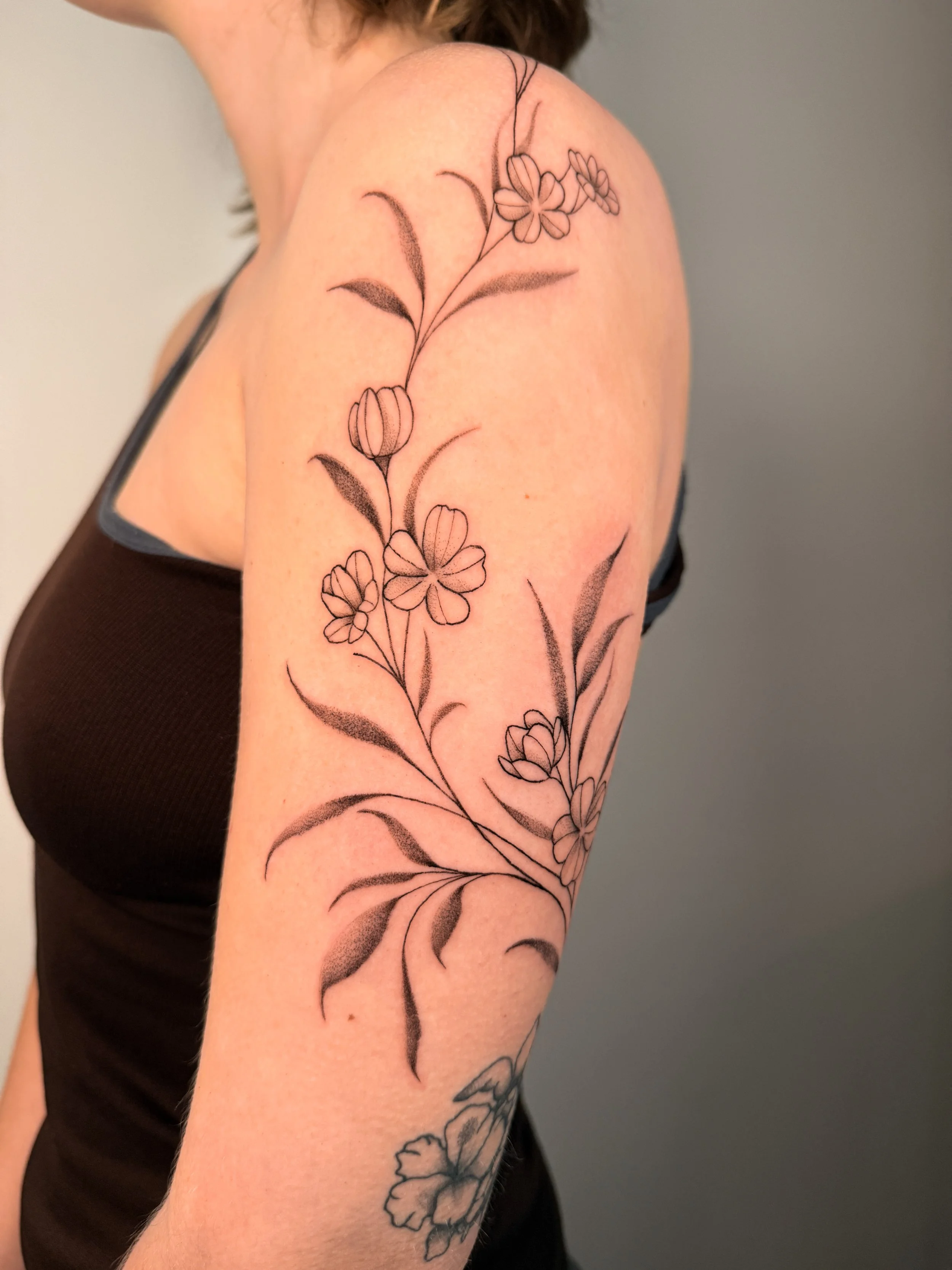 A black tattoo of flowers and leaves on someone's arm.