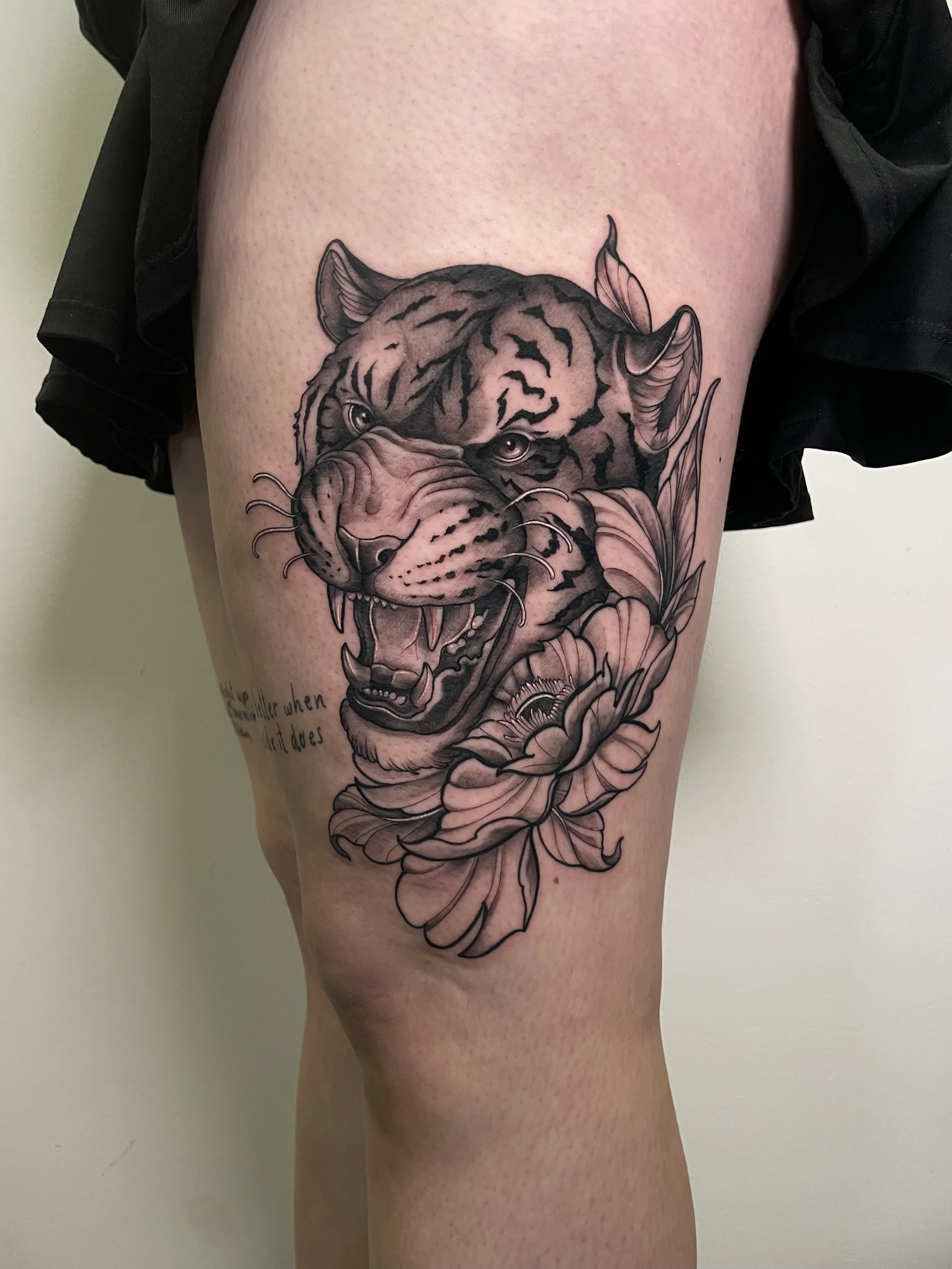 Tatouage d'une tête de tigre avec des fleurs autour, en noir et gris.