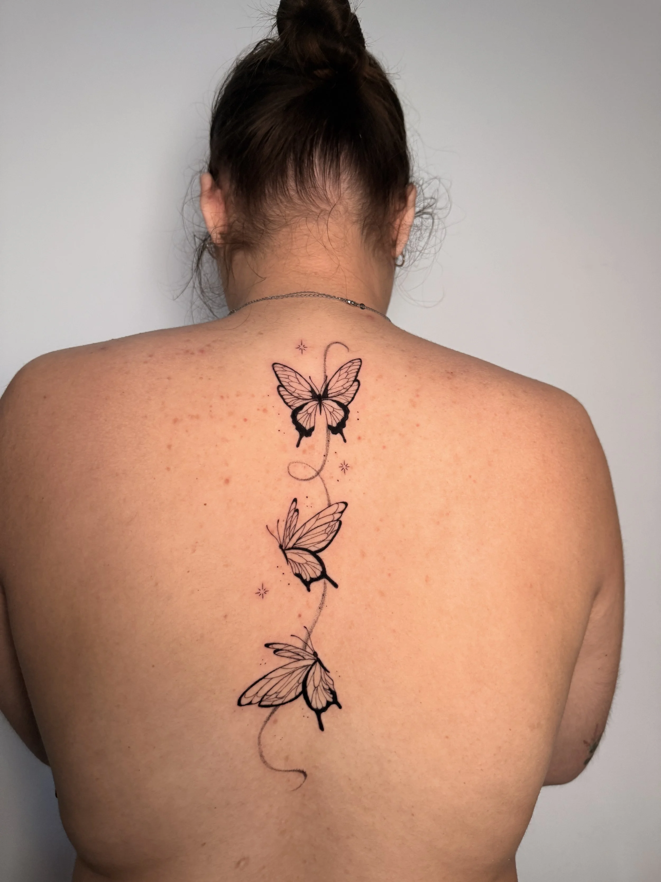 A tattoo of several black-and-white butterflies arranged vertically down a woman's back, starting at the top of her neck and extending down to the middle of her back.