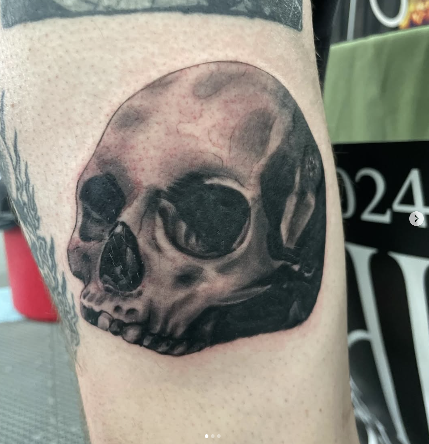 A black-and-gray tattoo of a human skull on the skin, located on the arm.