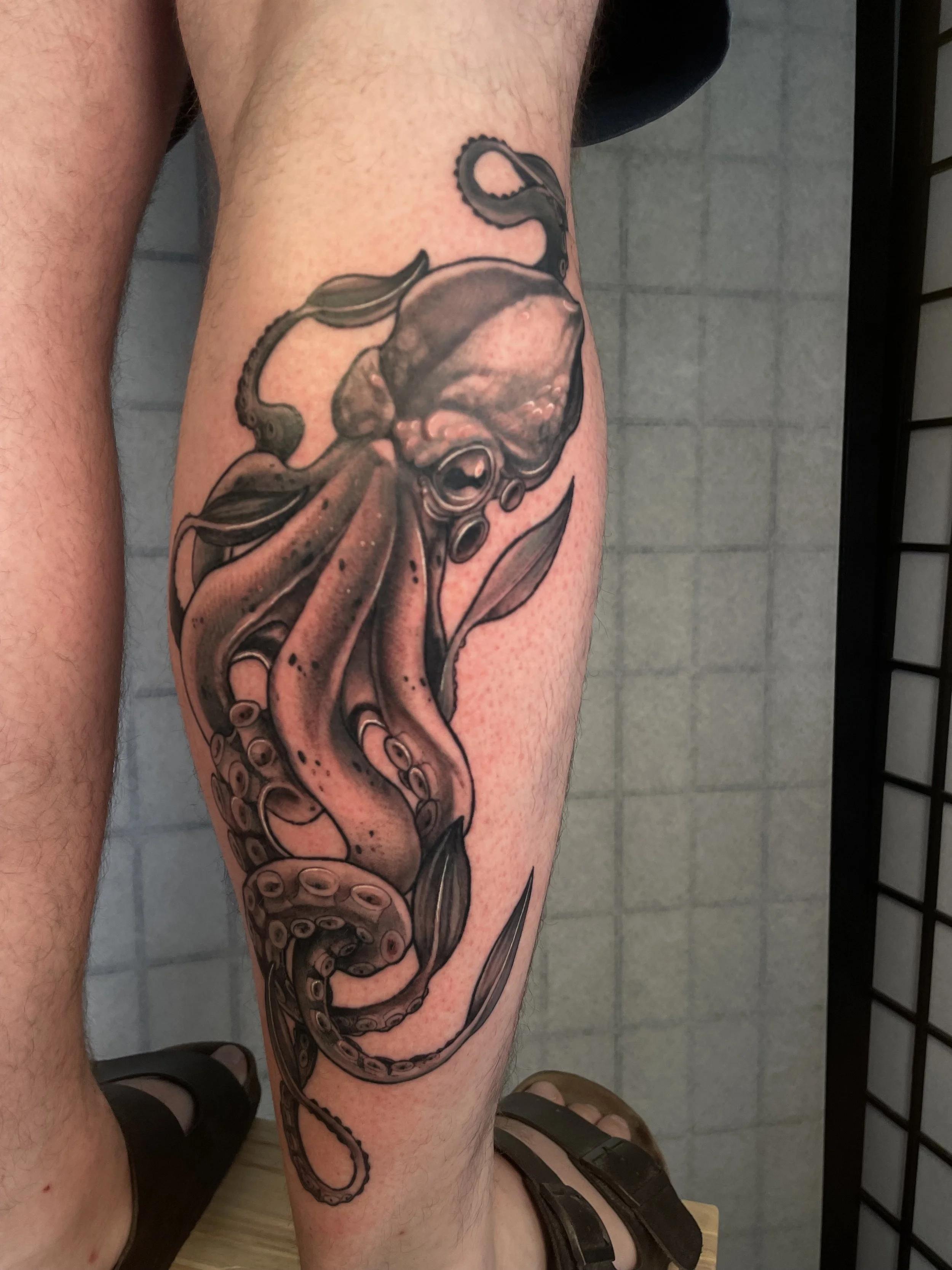 Tatouage d'un poulpe noir et gris sur la jambe d'une personne.