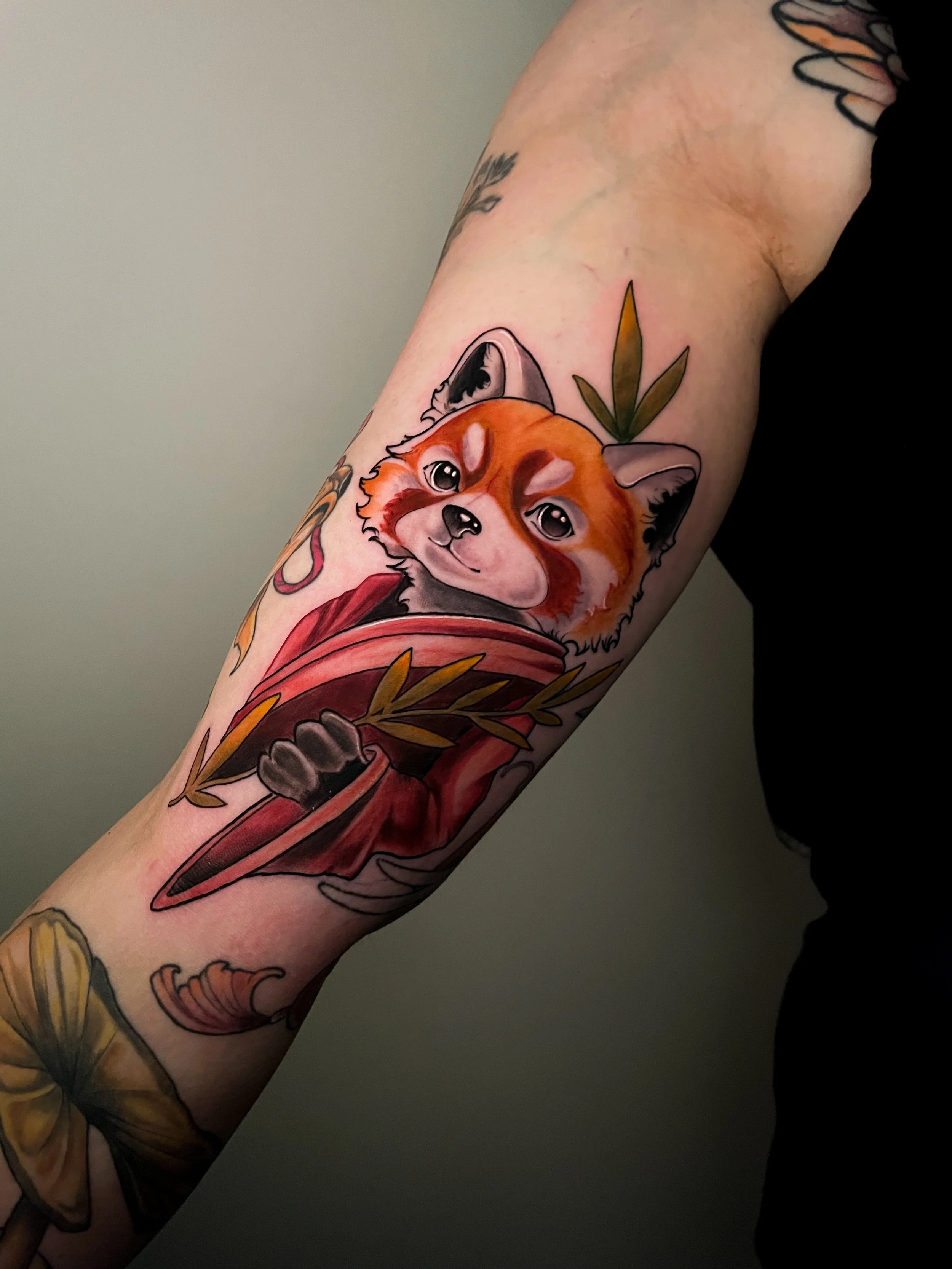 Tatouage d'un renard orange avec des yeux grands et un museau mignon, accompagné de feuilles vertes et de fleurs, sur un bras