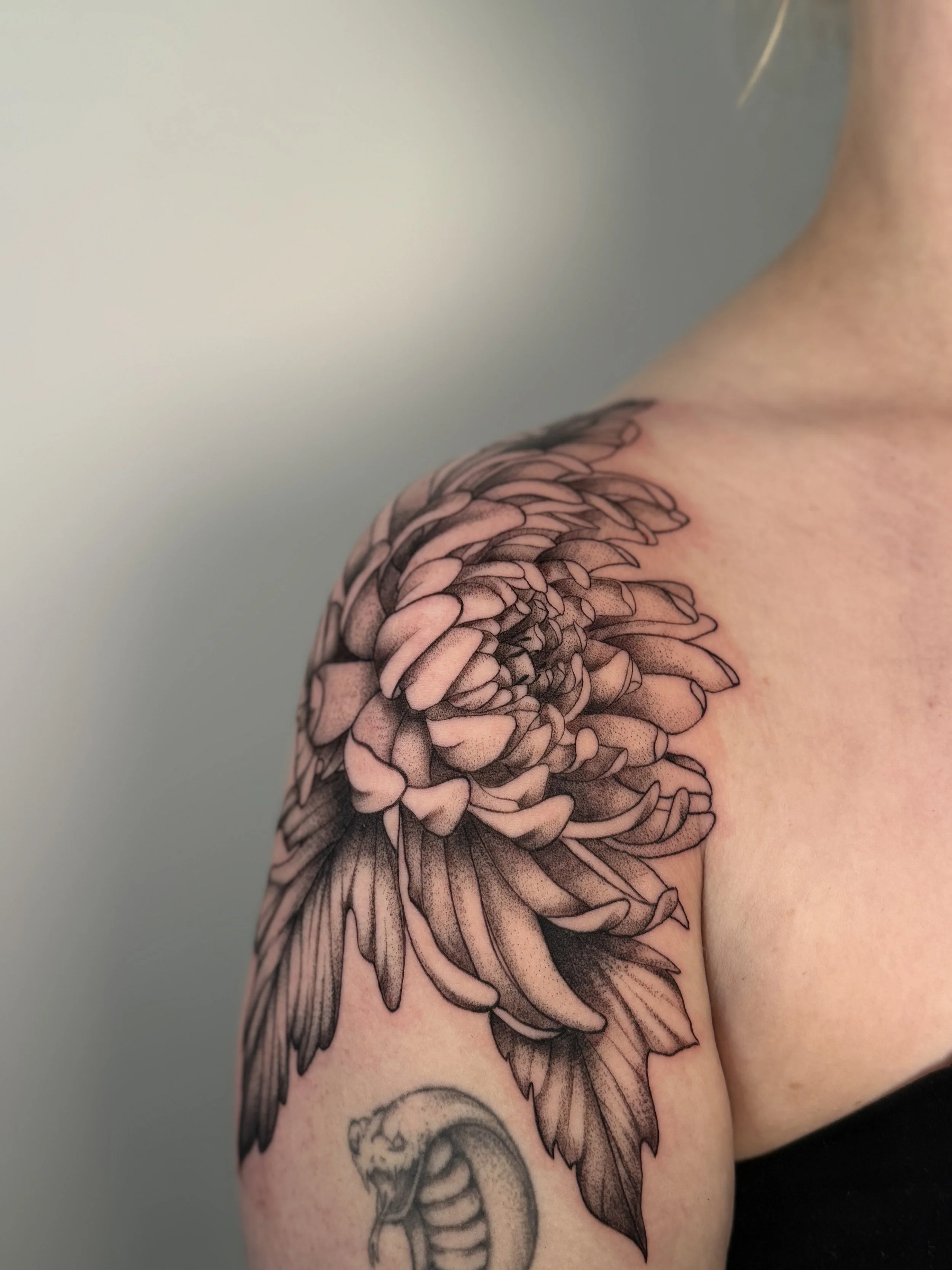 Tattoo of a large flower on the shoulder, with a snake underneath.