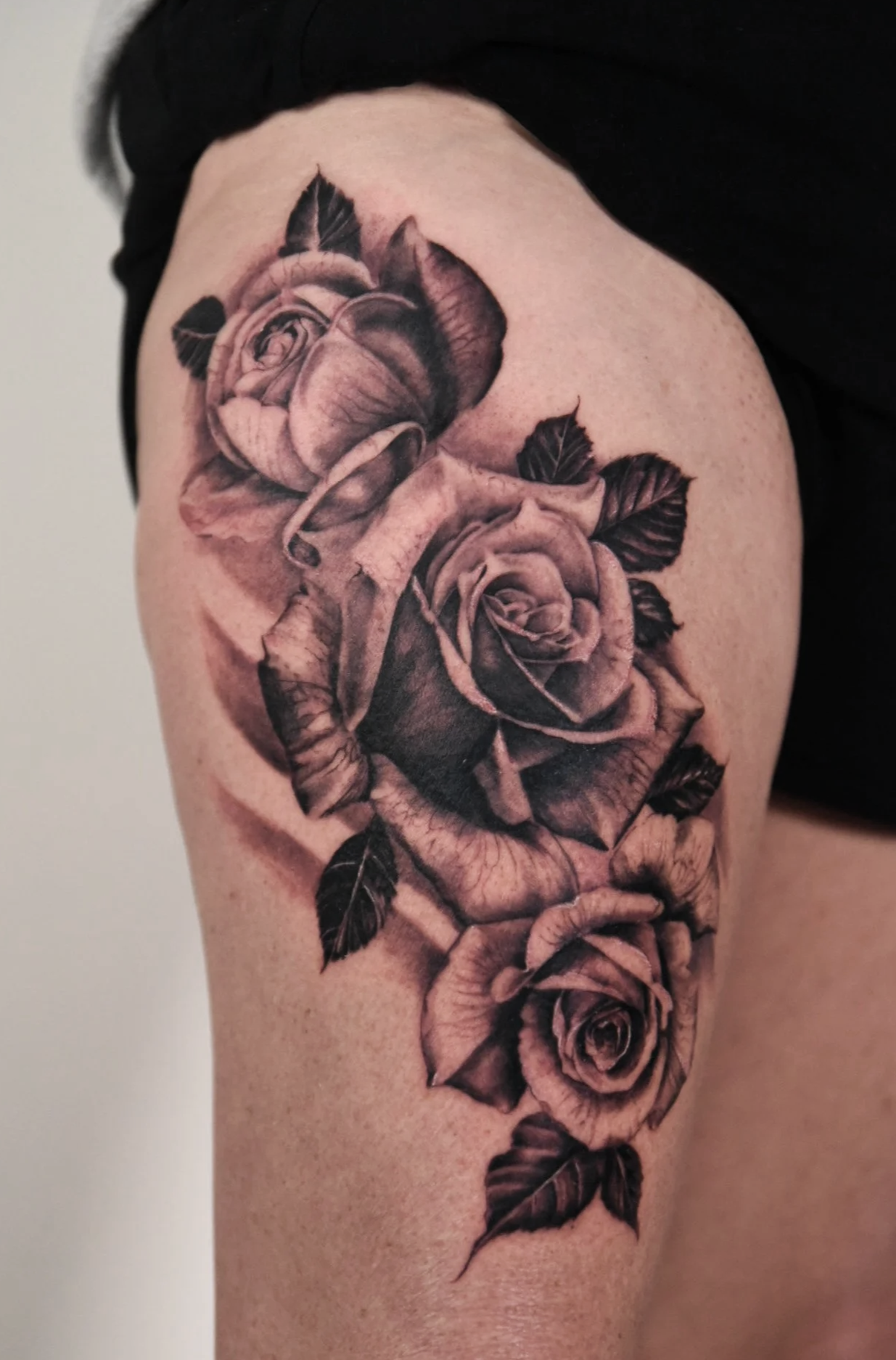 Black and gray tattoo of three roses on the arm.