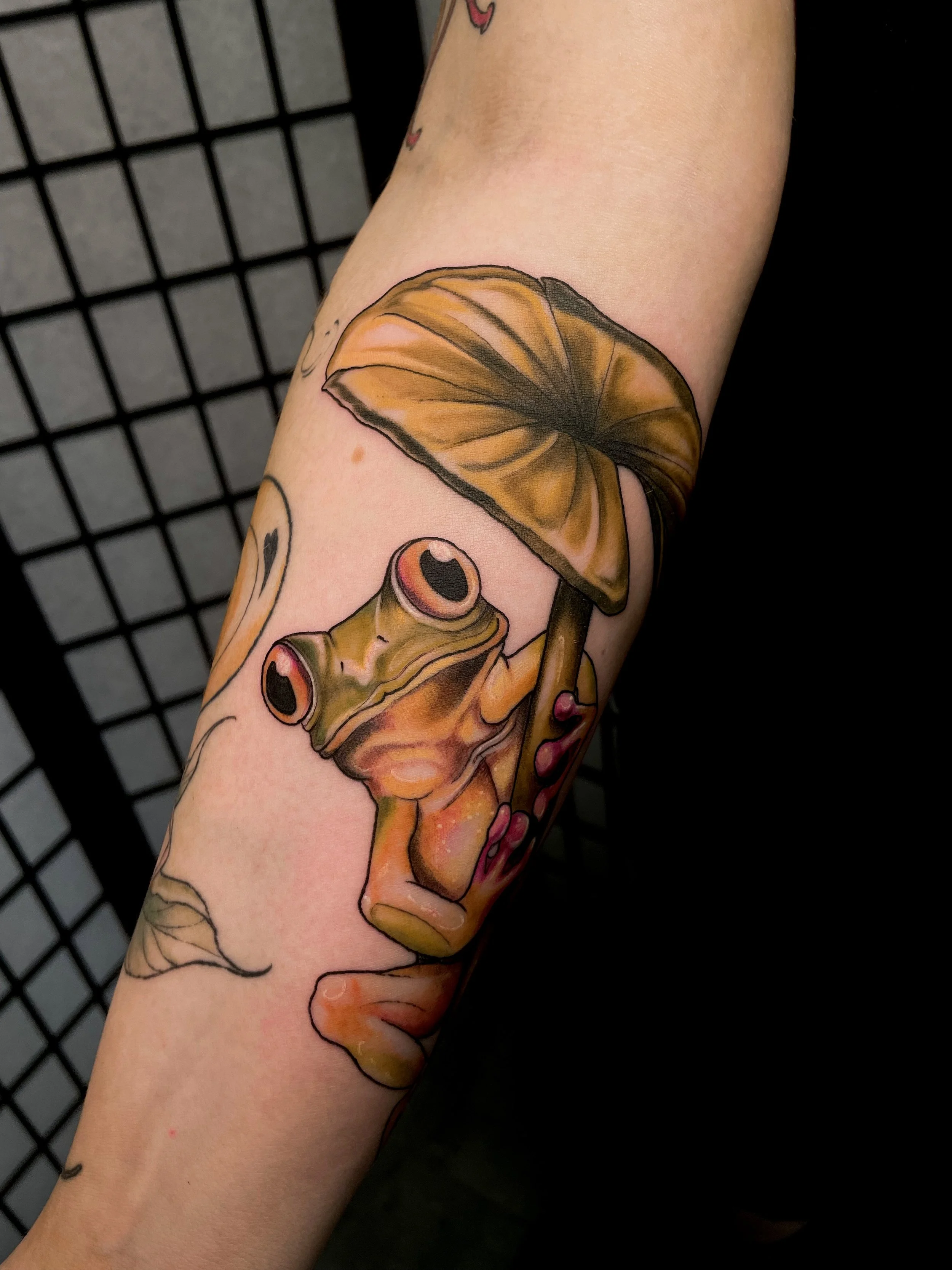 Tattoo of a frog under a mushroom on the arm.