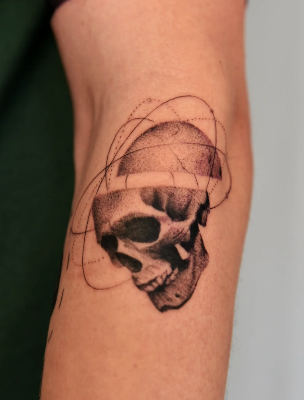 Black and white tattoo of a human skull, combined with geometric lines and abstract shapes, on the arm.