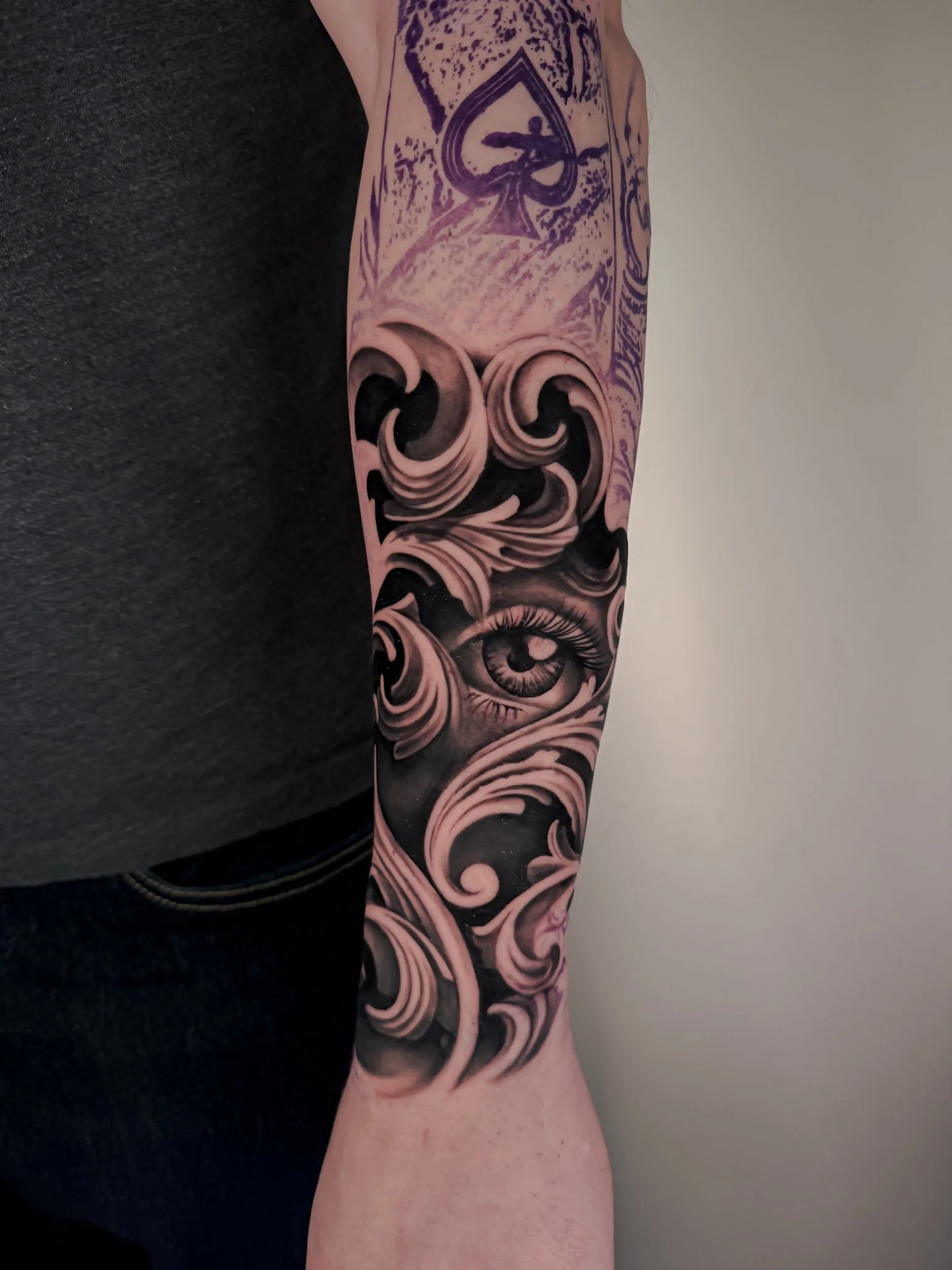 A black-and-gray tattoo of a stylized human figure inside a heart-shaped frame on the arm