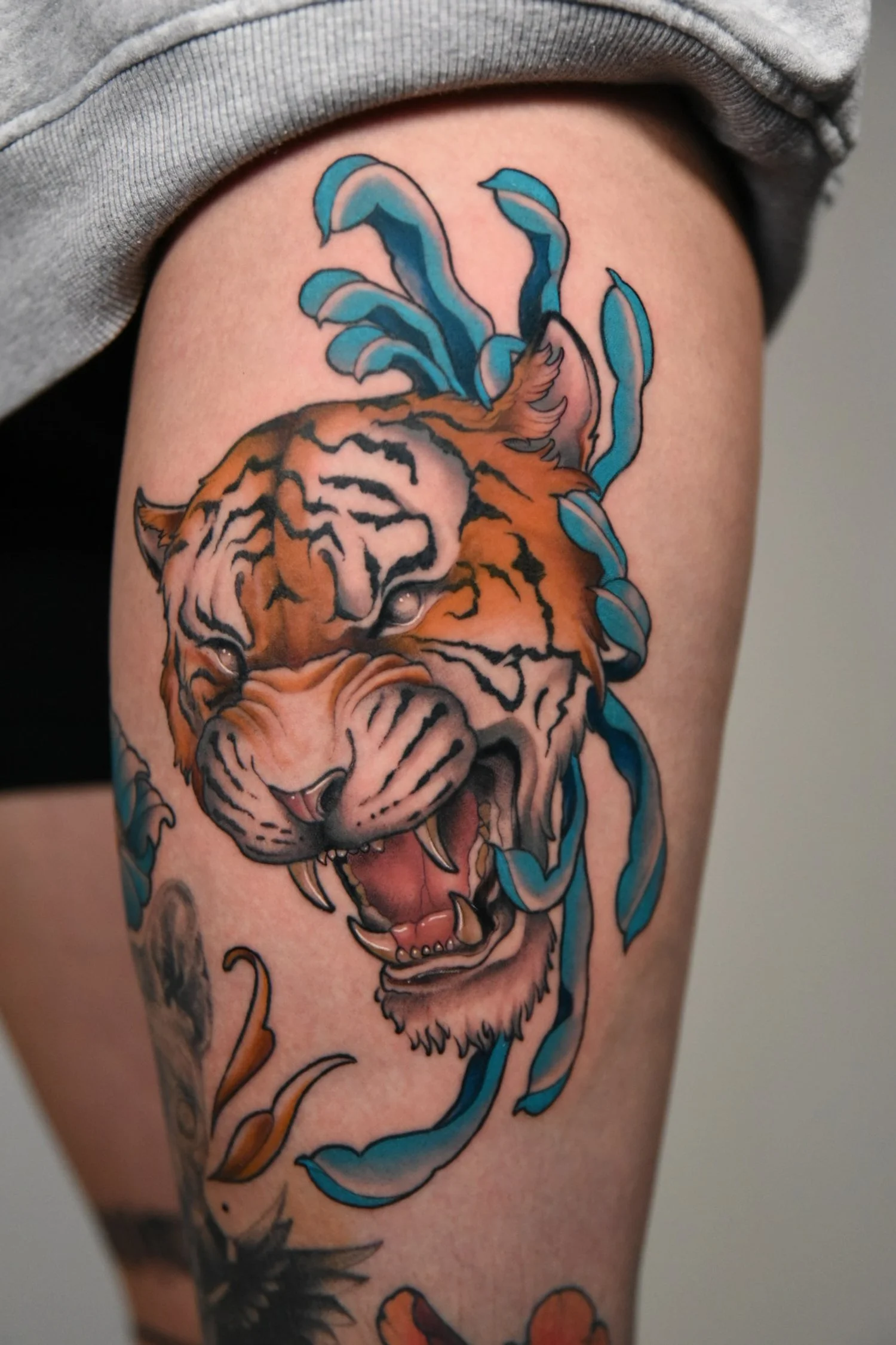 Realistic tiger head tattoo with black and orange stripes, surrounded by blue ribbons.