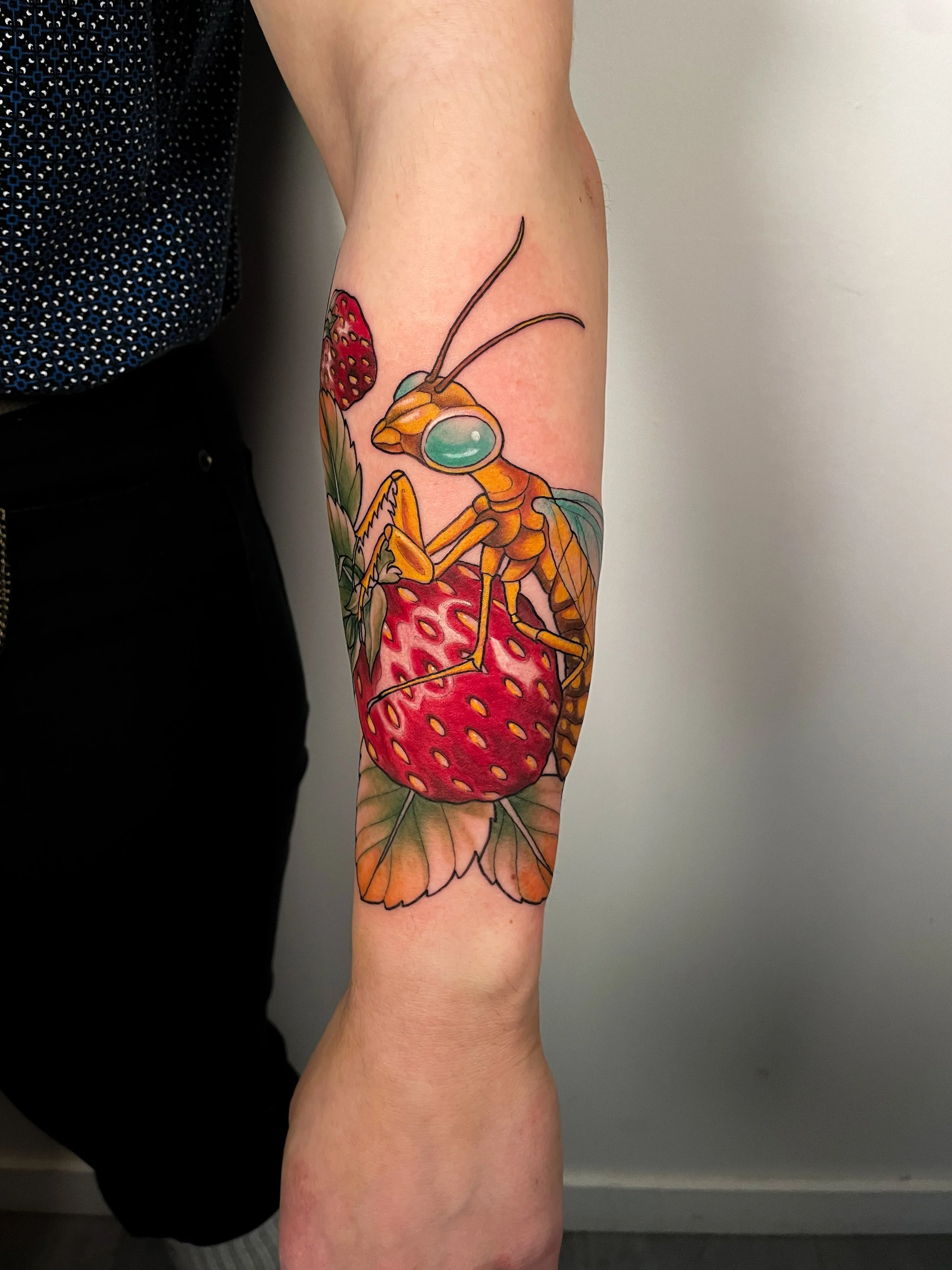 Tattoo of a bee on a strawberry, with green leaves and a red mushroom with white dots.