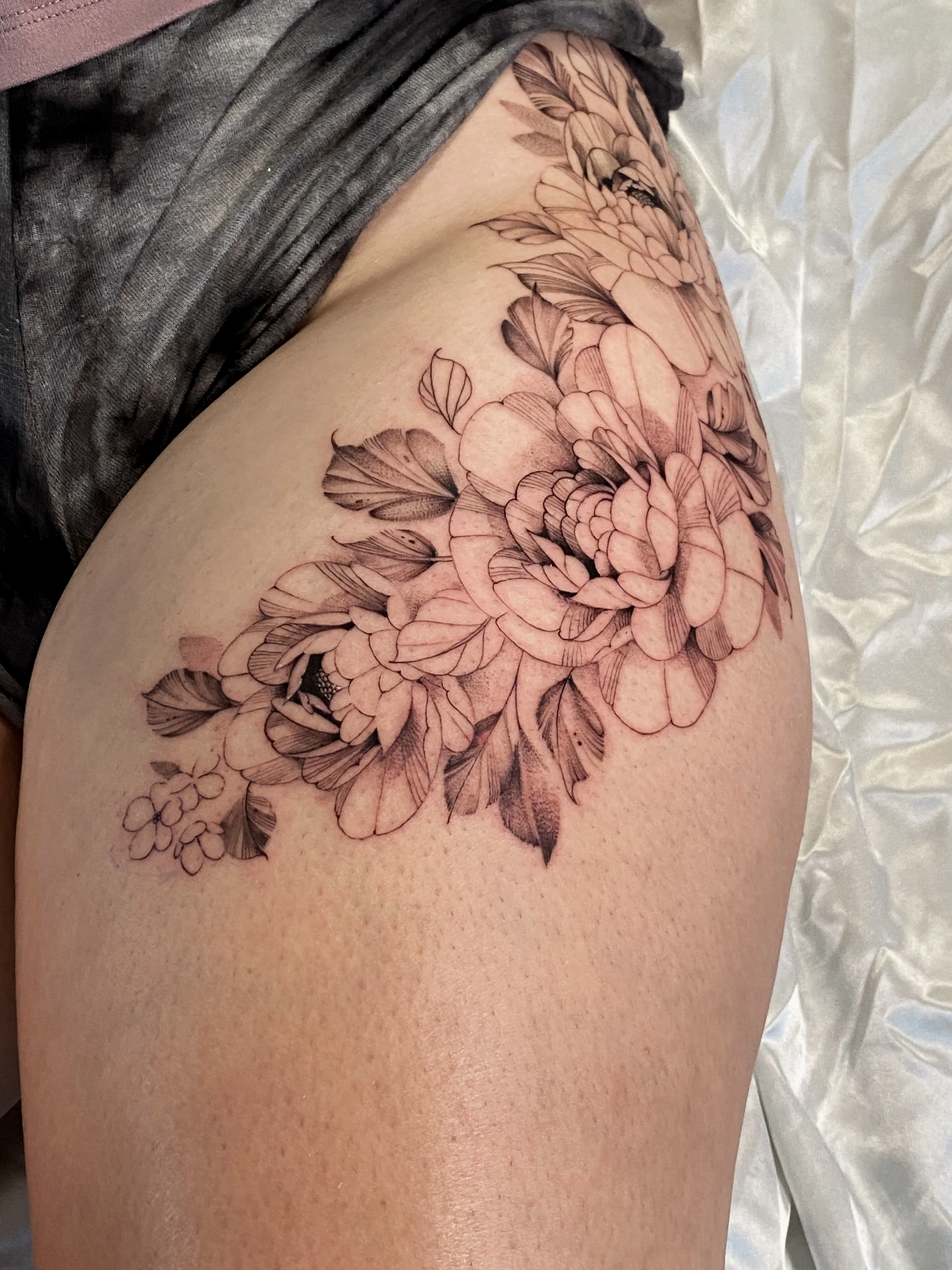 Black and gray flower tattoo on a person's thigh.