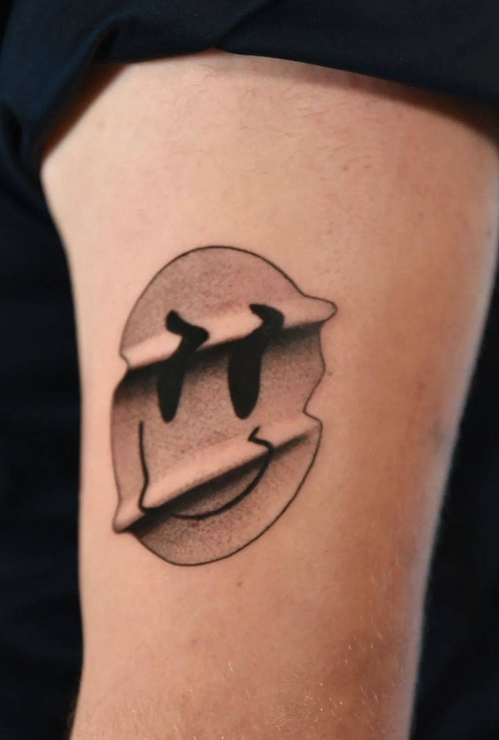 Tattoo of a smiling face with abstract design and tear-shaped eyes.