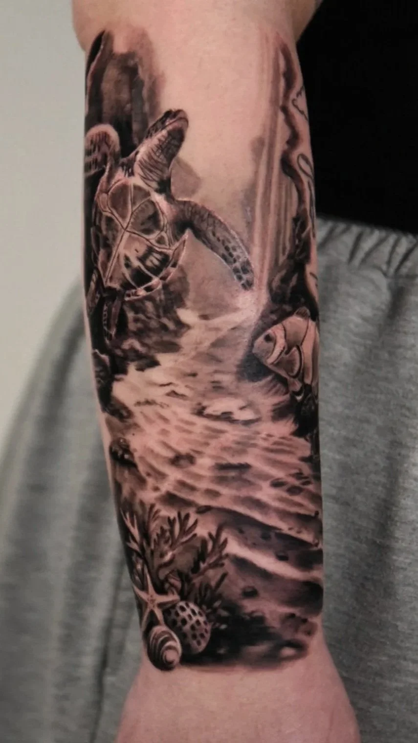 Black and gray tattoo of a sea turtle swimming in the ocean, with elements like seaweed, a starfish, shells and rocks.