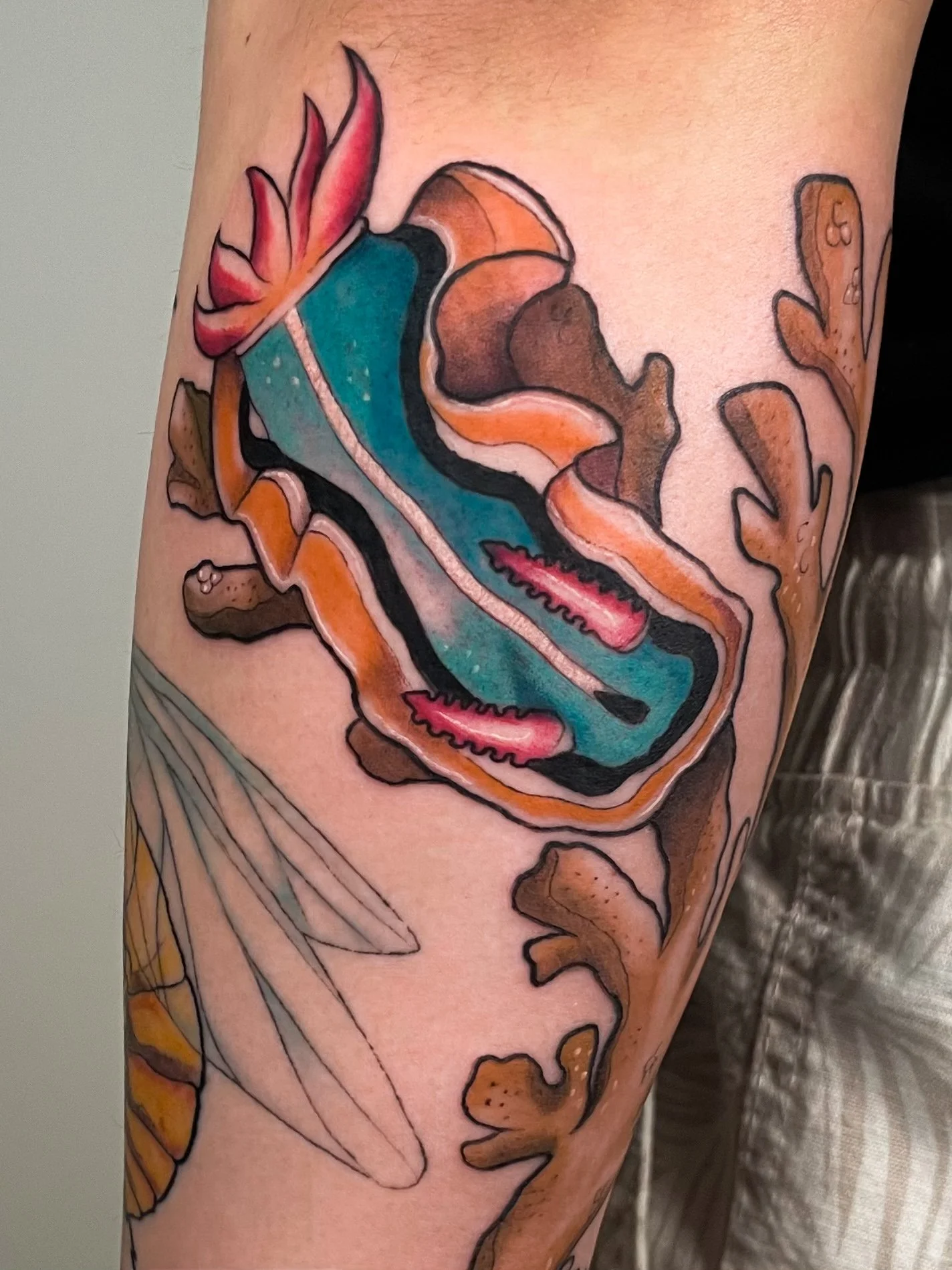 Colorful tattoo of a blue and orange shoe, surrounded by plants and leaves.