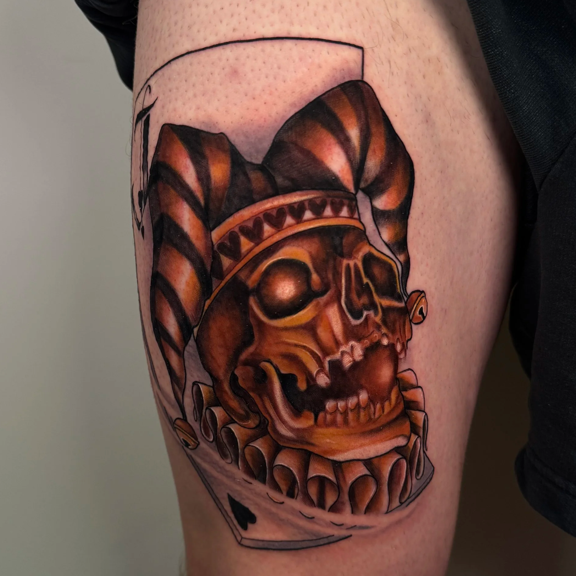 Tattoo of a skull with horns, decorated with a headband with hearts, in a dark, detailed style, placed on the thigh.