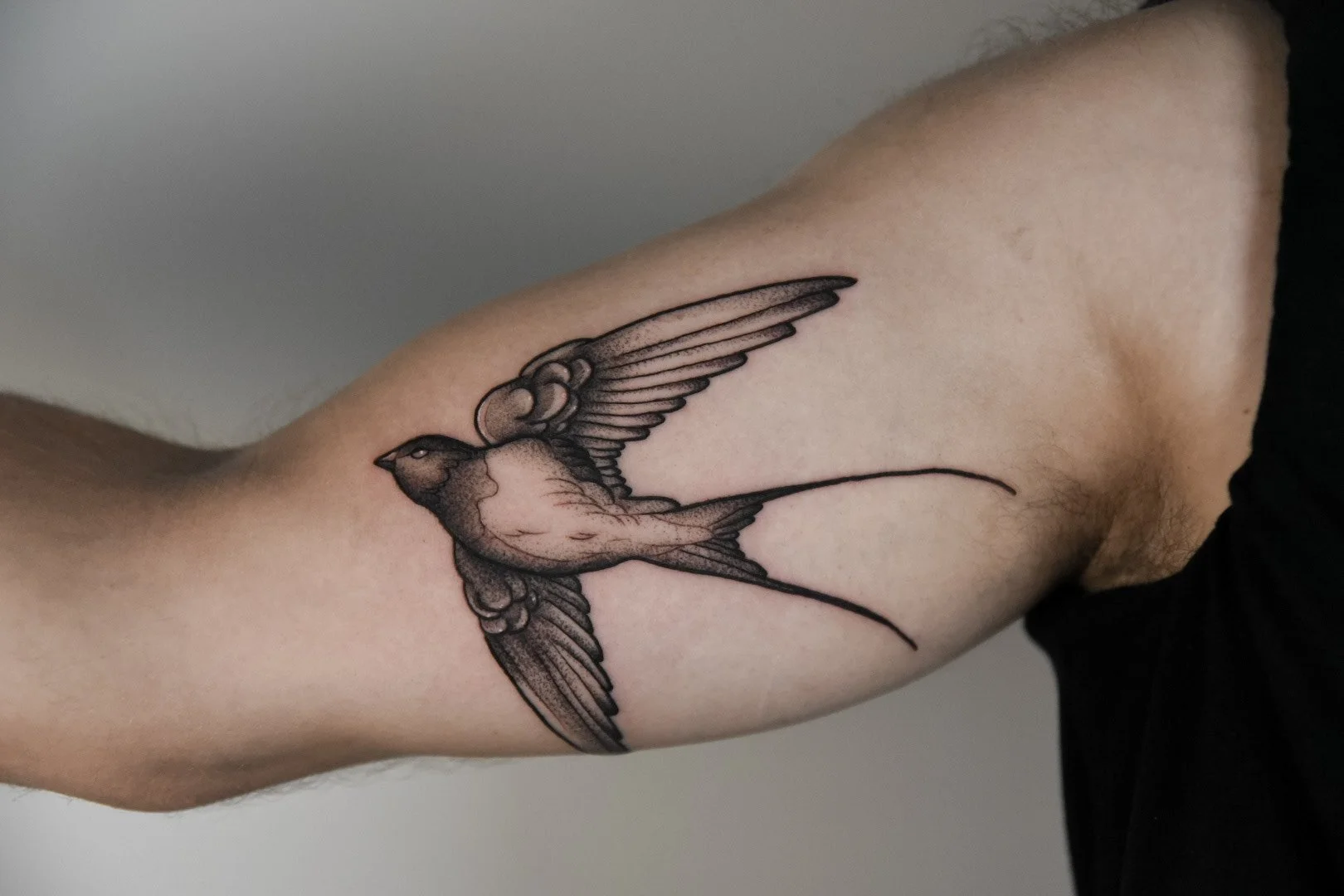 Tattoo of a swallow on a muscular arm.