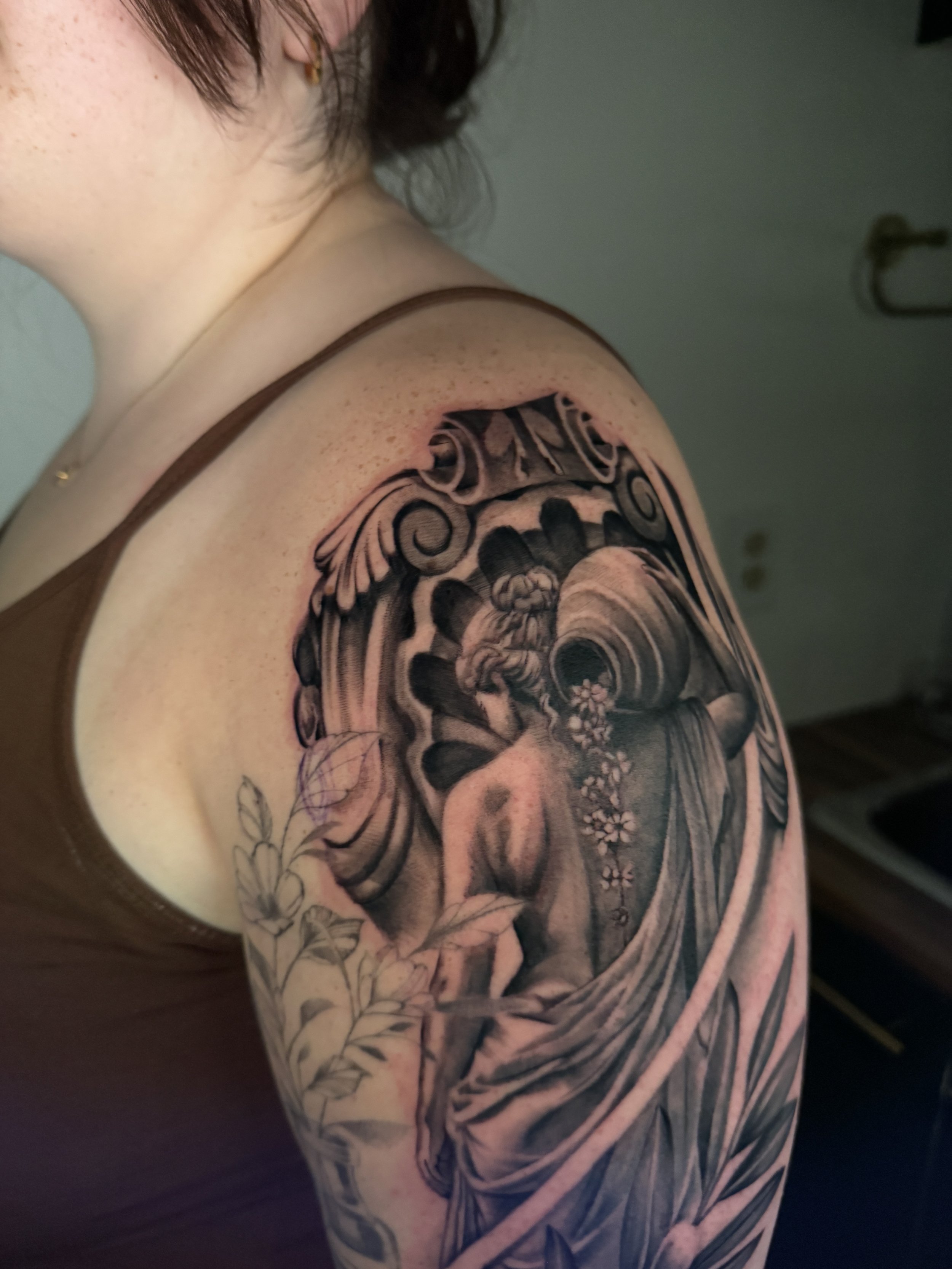 An arm featuring an intricate Japanese-style tattoo, including flowers, clouds, and traditional motifs, in black and gray.