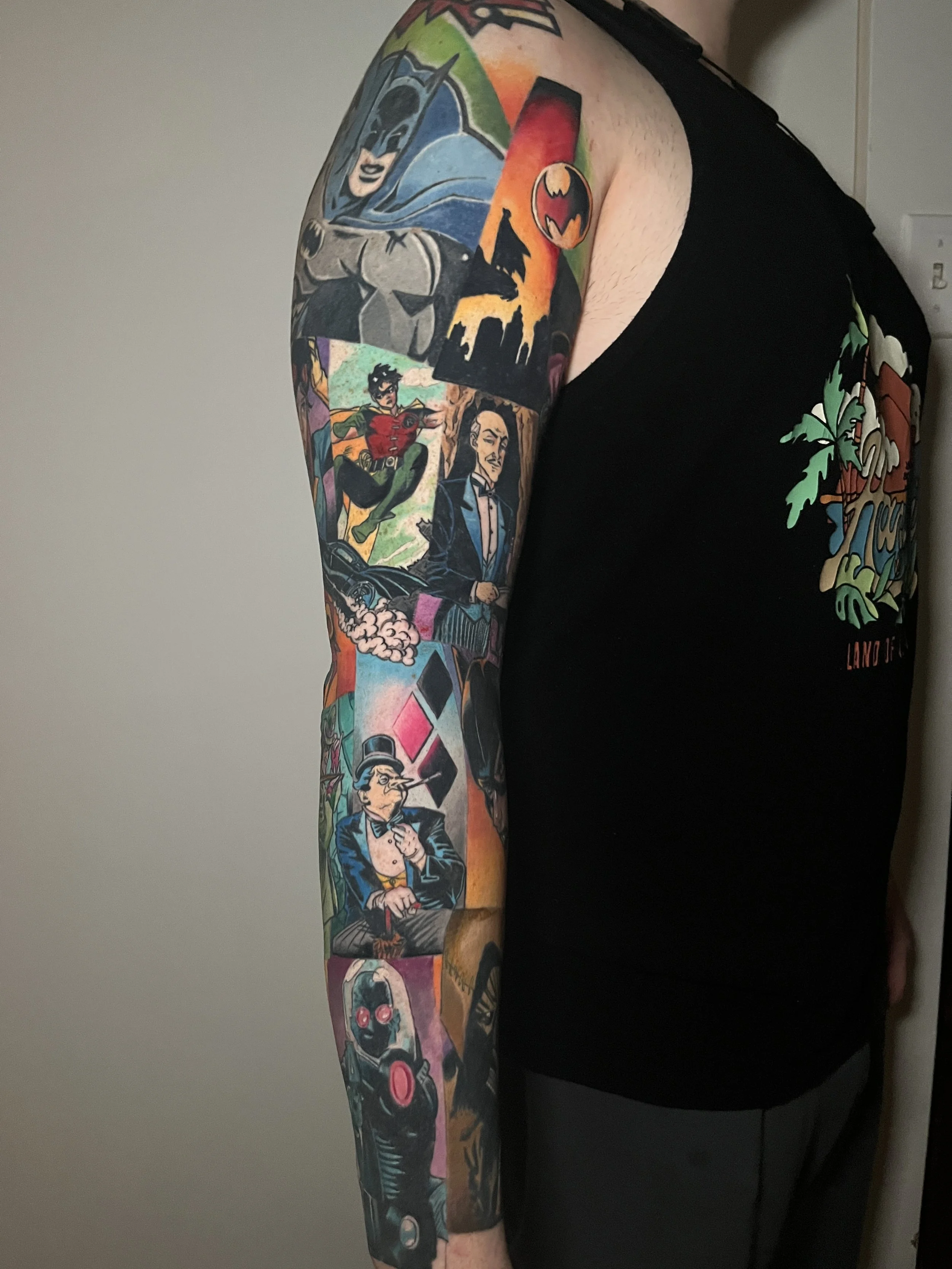 Colorful tattoo on a man's arm, depicting characters and symbols from pop culture and comic books.